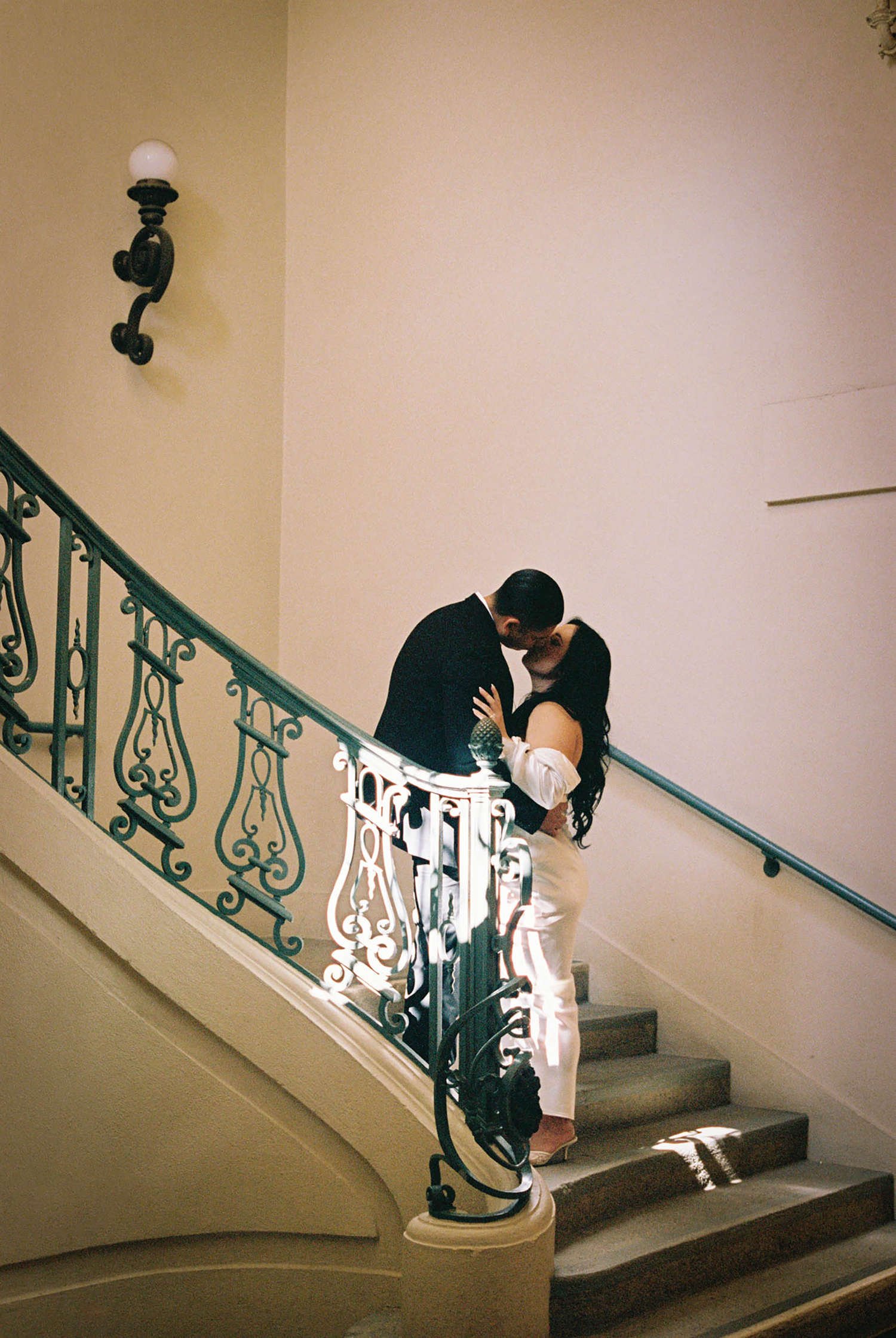 Couple sharing a kiss on elegant green wrought iron staircase in a classic interior.