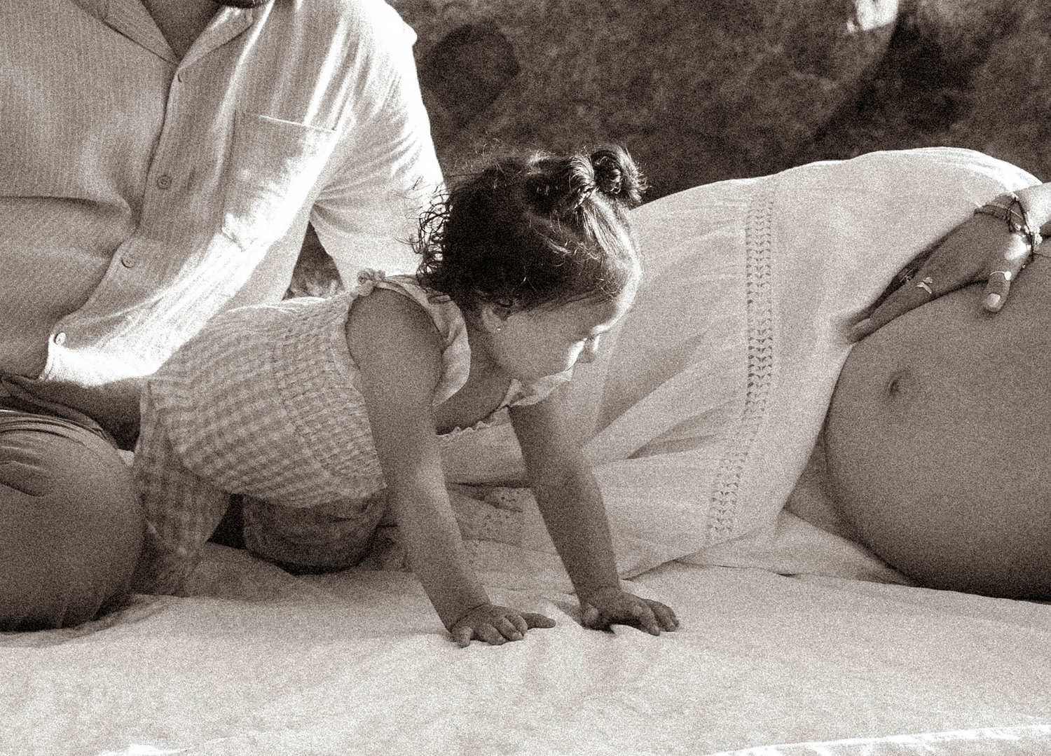 Black and white photo of a toddler crawling near a pregnant woman's belly during a maternity photoshoot.