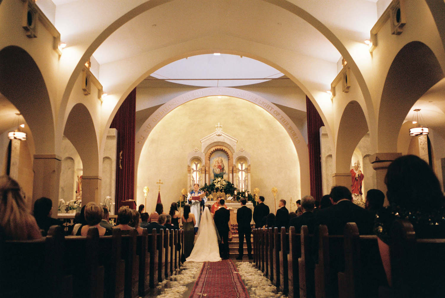 Wedding ceremony inside elegant arched church with guests seated in pews as couple stands at floral altar.