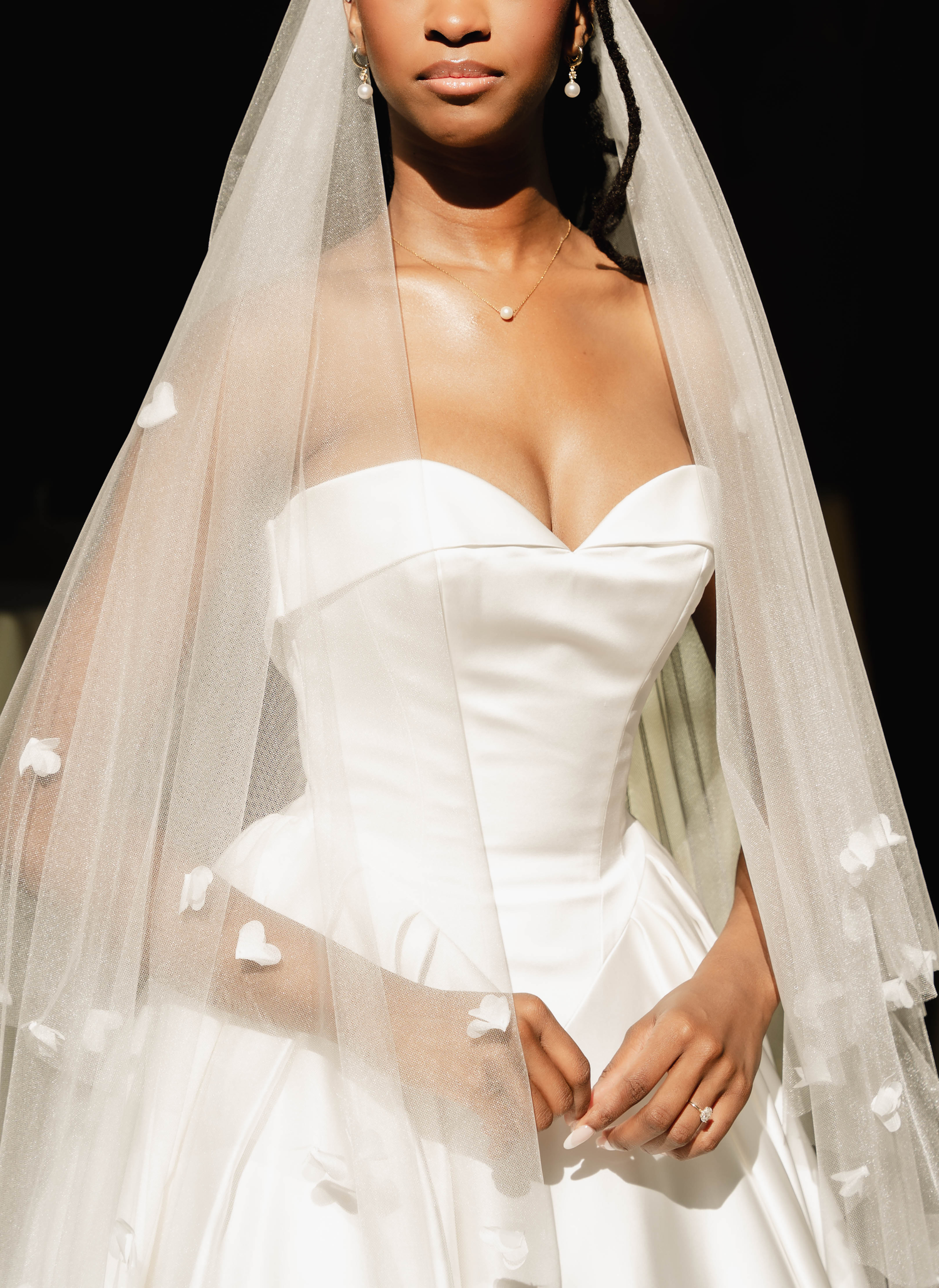Bride wearing a strapless white satin wedding gown with peplum waist and floral-trimmed cathedral veil.