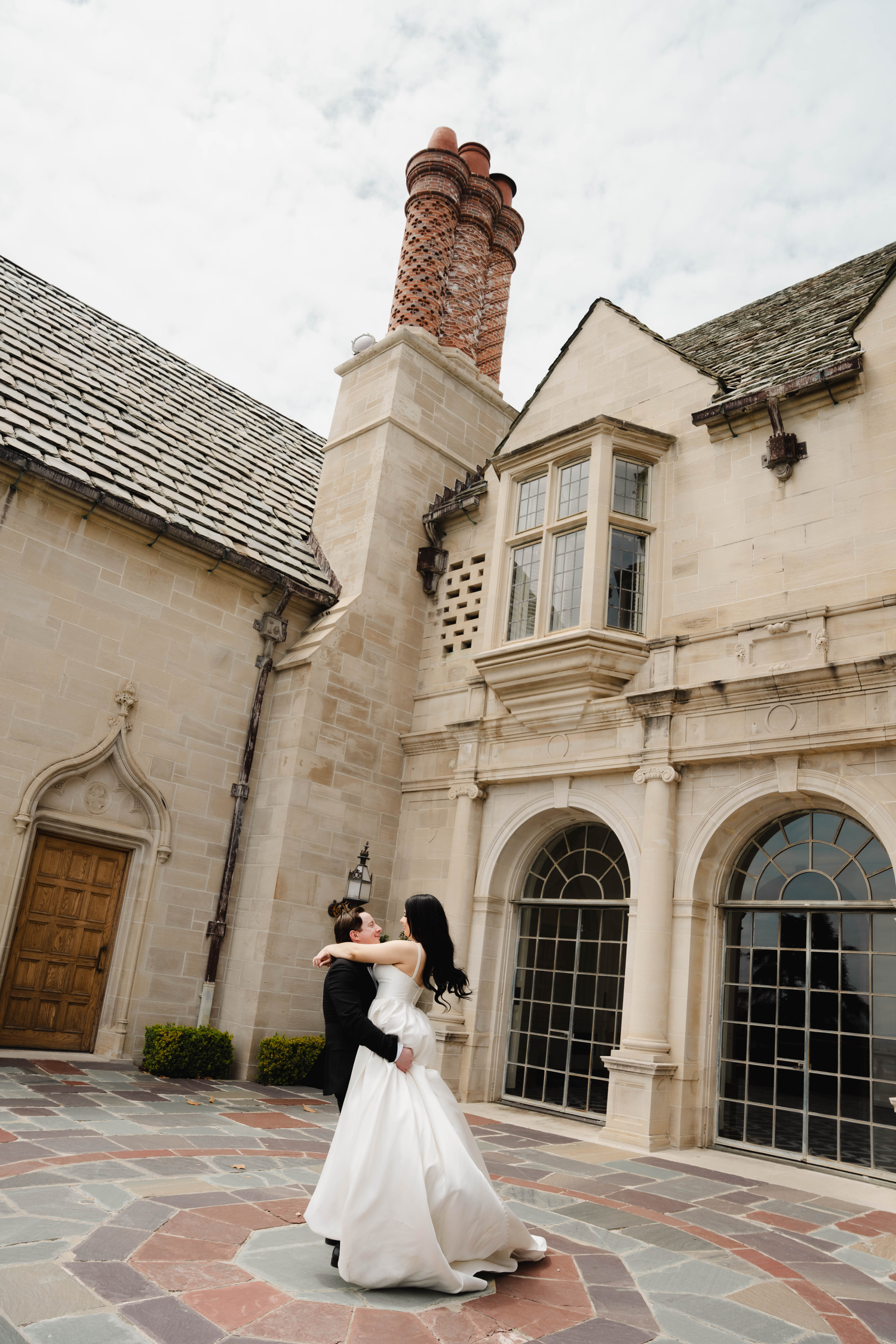 Bride and groom embrace in a romantic dance in the courtyard of an elegant stone mansion on their wedding day.