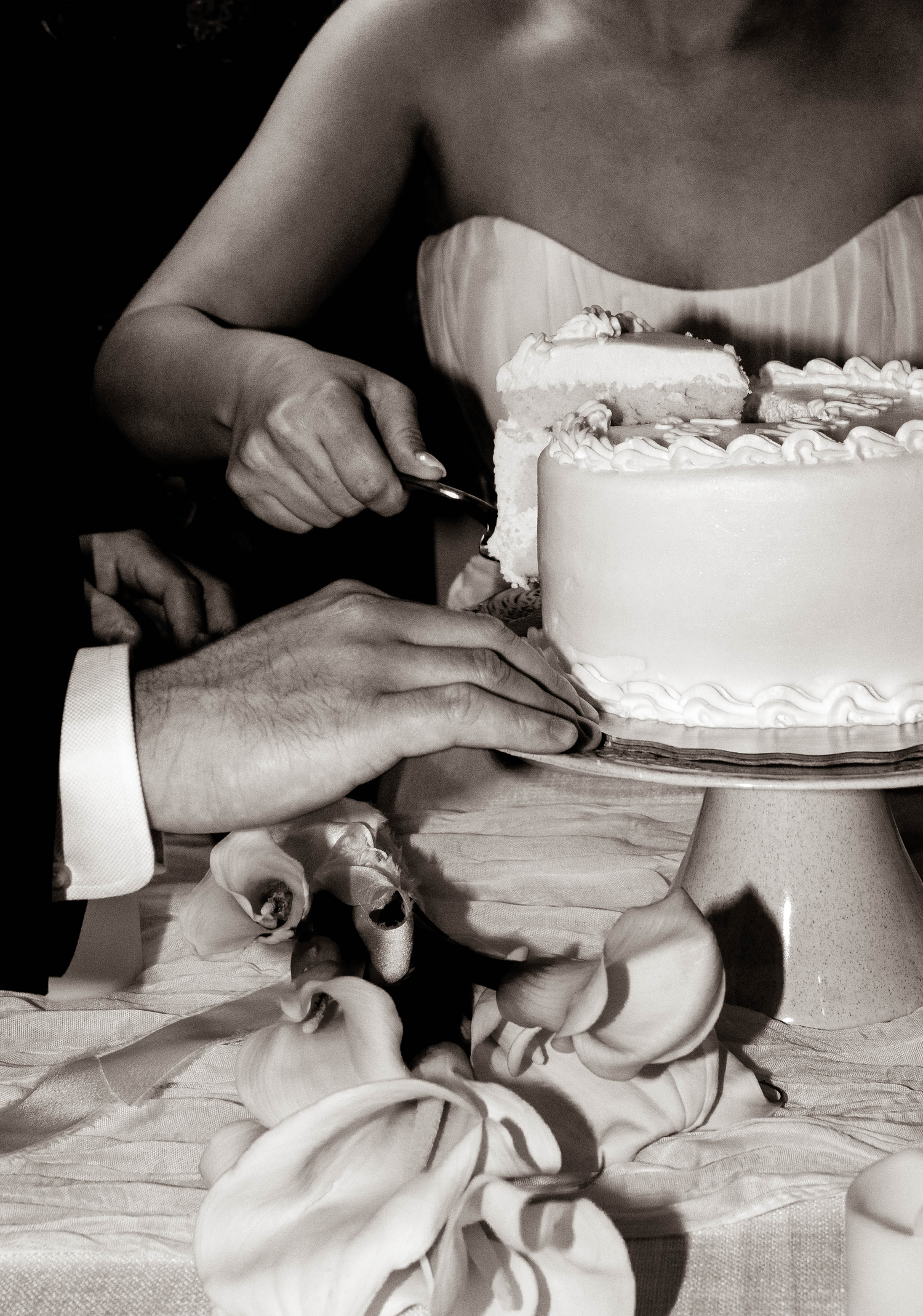 Black and white photo of bride and groom cutting their white tiered wedding cake adorned with flowers.
