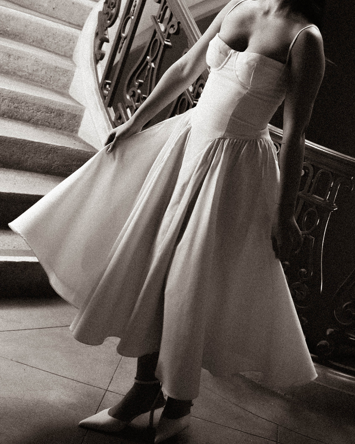 Black and white photo of elegant bride in structured corset ball gown on ornate staircase.