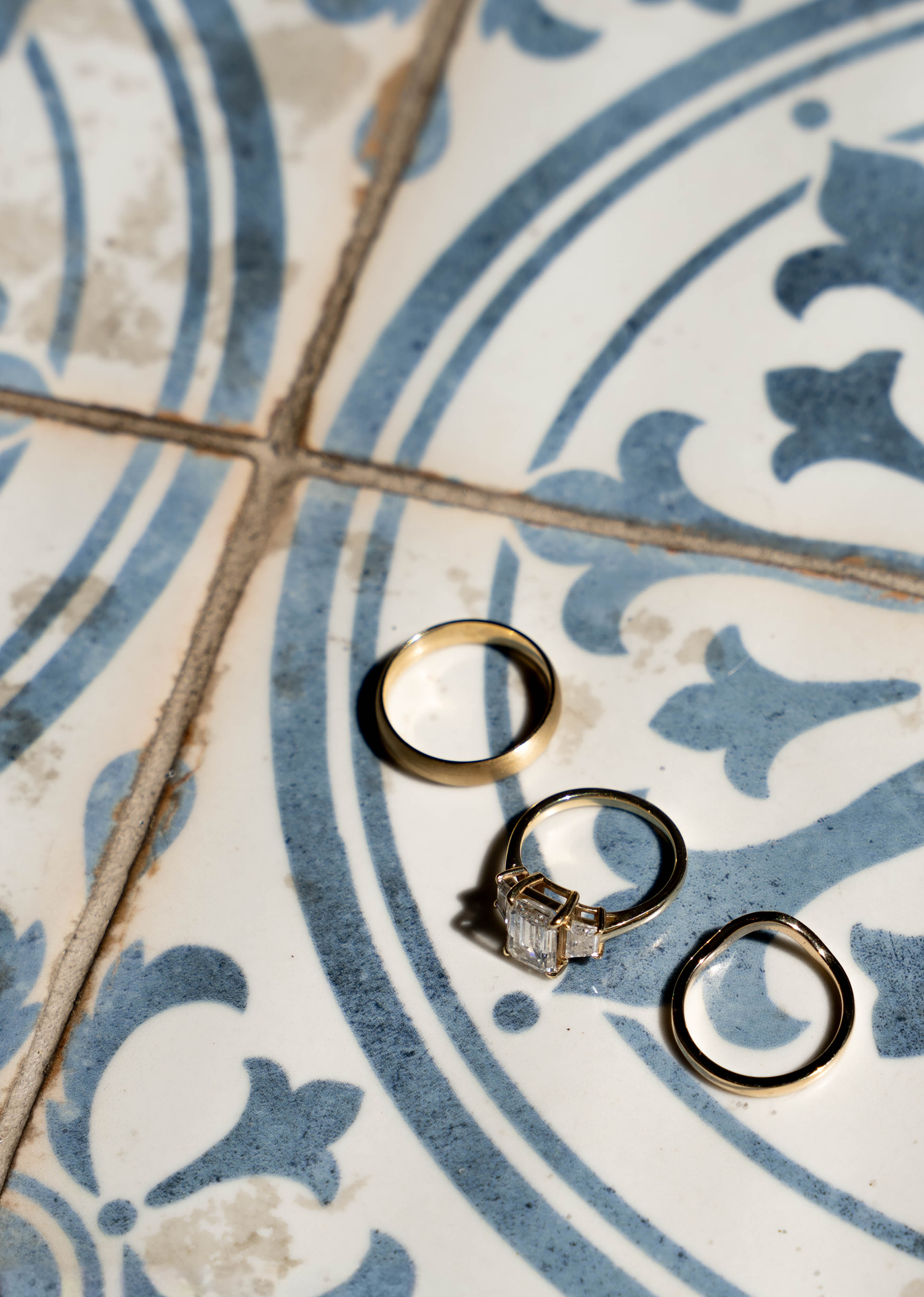 Three gold wedding rings displayed on decorative blue and white patterned ceramic tiles, including a diamond engagement ring.