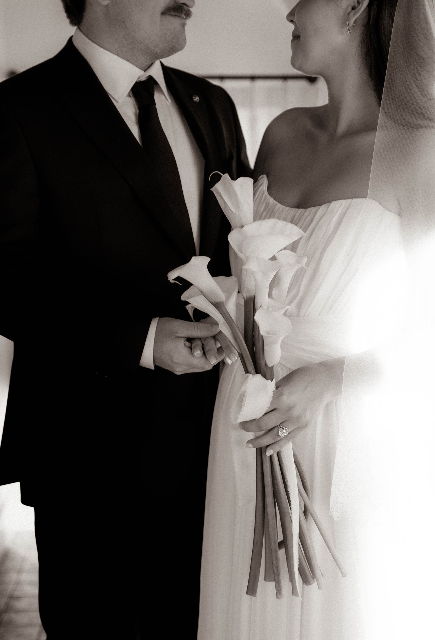 Black and white photo of bride and groom holding calla lily bouquet.