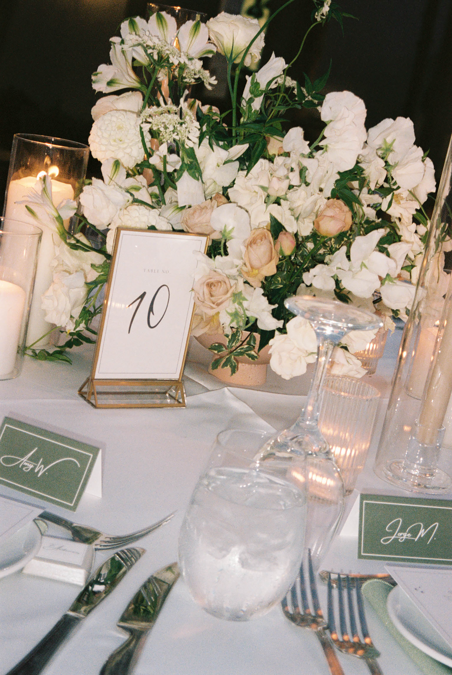 Elegant wedding reception table with white floral centerpiece, candles, crystal glassware, and gold table number 10.