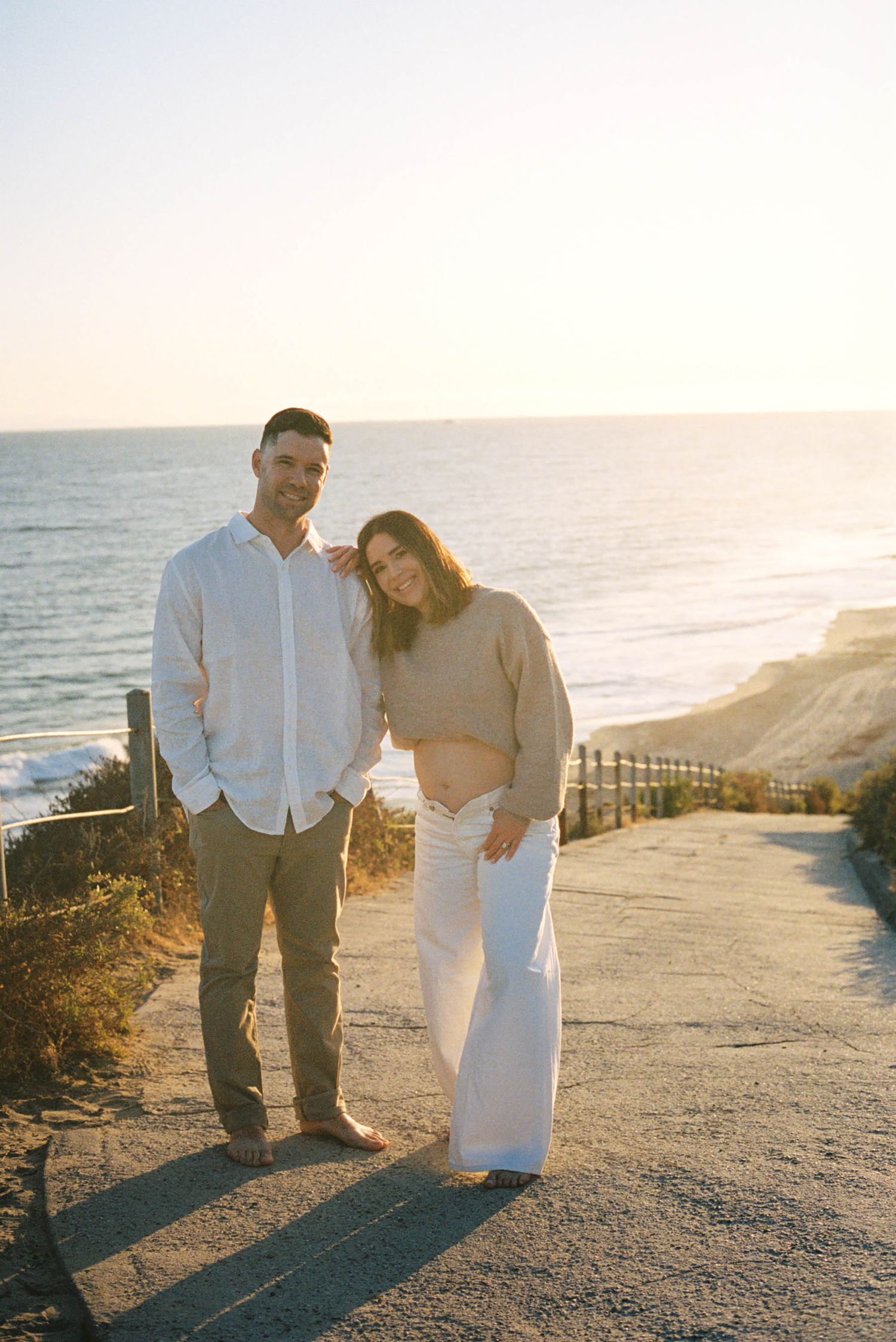 Couple posing together on a coastal cliffside path at golden hour with ocean views in the background.