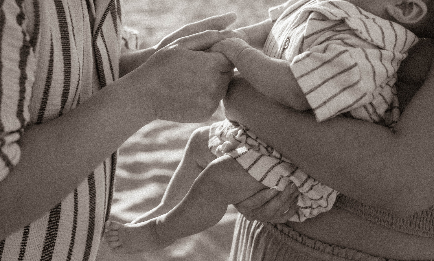 Adult hands gently holding a newborn baby wrapped in a striped blanket in a tender black and white photo.