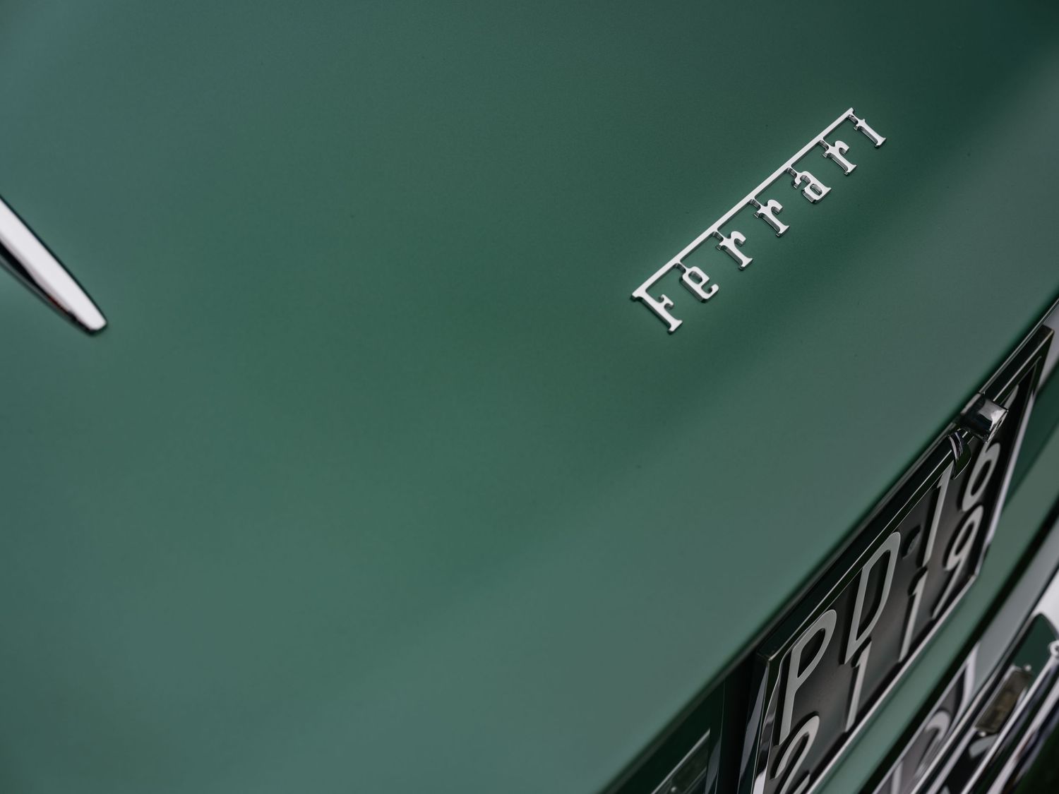 Close-up of a green Ferrari hood featuring the iconic silver Ferrari script logo on a luxury sports car.