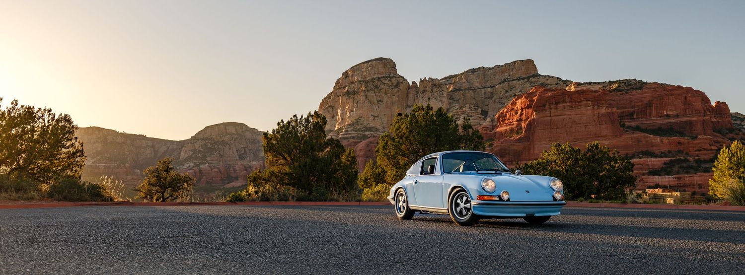 A vintage blue Porsche 911 parked on a desert road with stunning red rock formations at sunset in Sedona, Arizona.