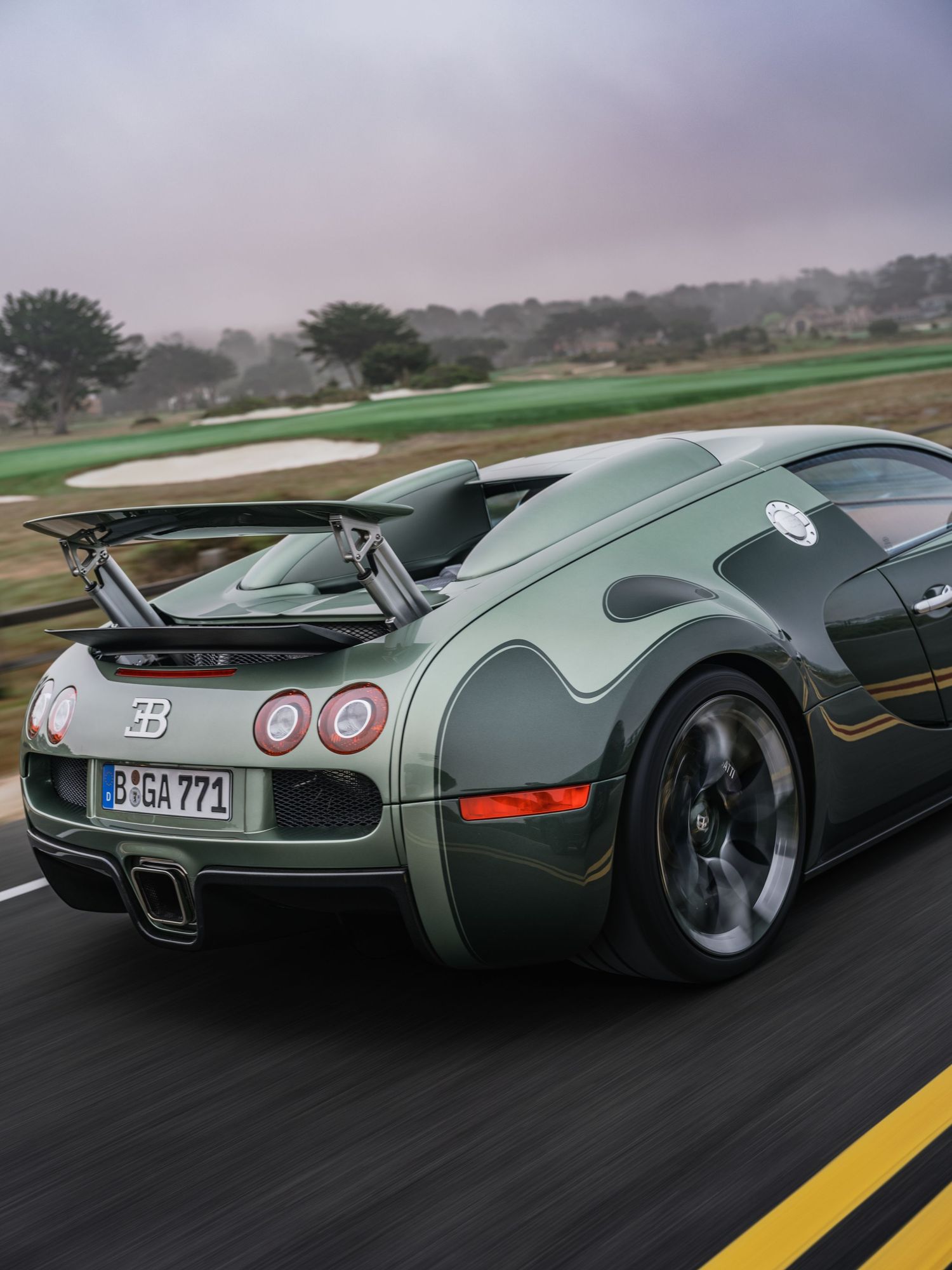 Green Bugatti Veyron Grand Sport supercar speeding on a racetrack with rear spoiler raised, license plate BGA 771.