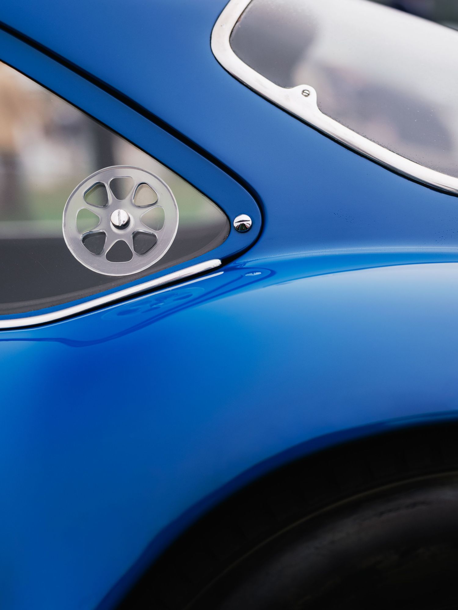 Close-up of a vibrant blue classic car featuring a chrome fuel cap and sleek curved bodywork.