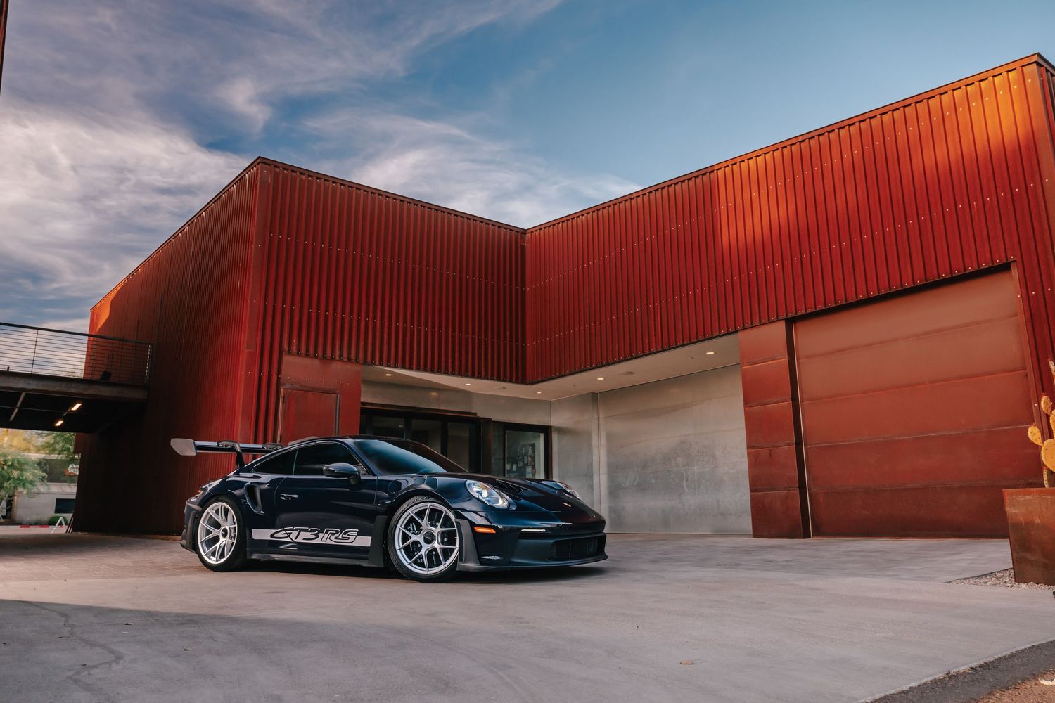 Black Porsche 911 GT3 parked in front of a modern red metal building with a large garage door.