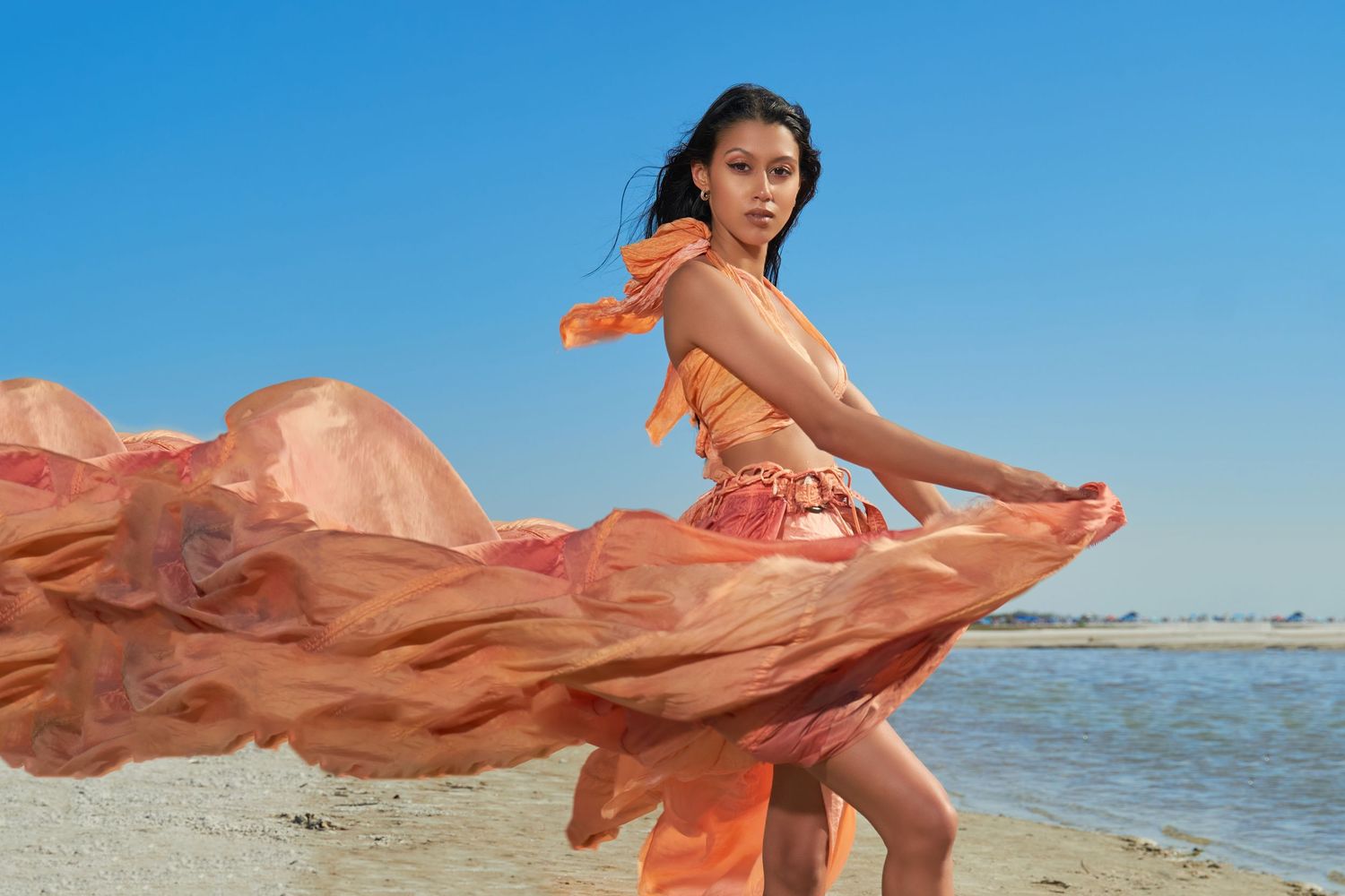 Coral fabric billowing dramatically against beach and ocean backdrop.