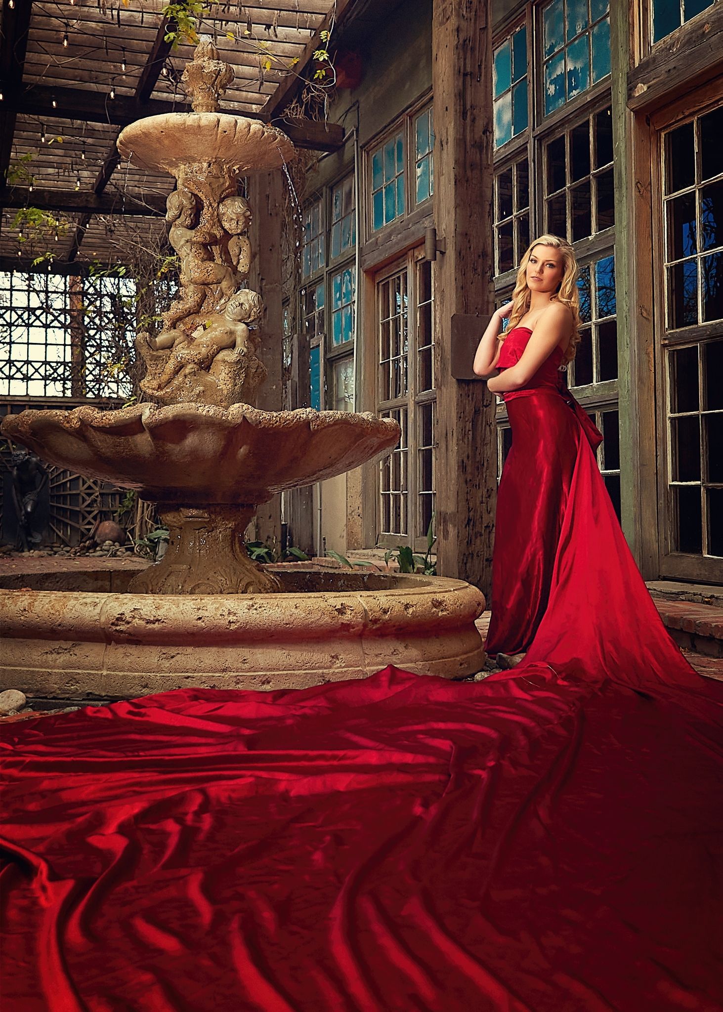 Flowing red gown with long train photographed in dramatic abandoned building setting.