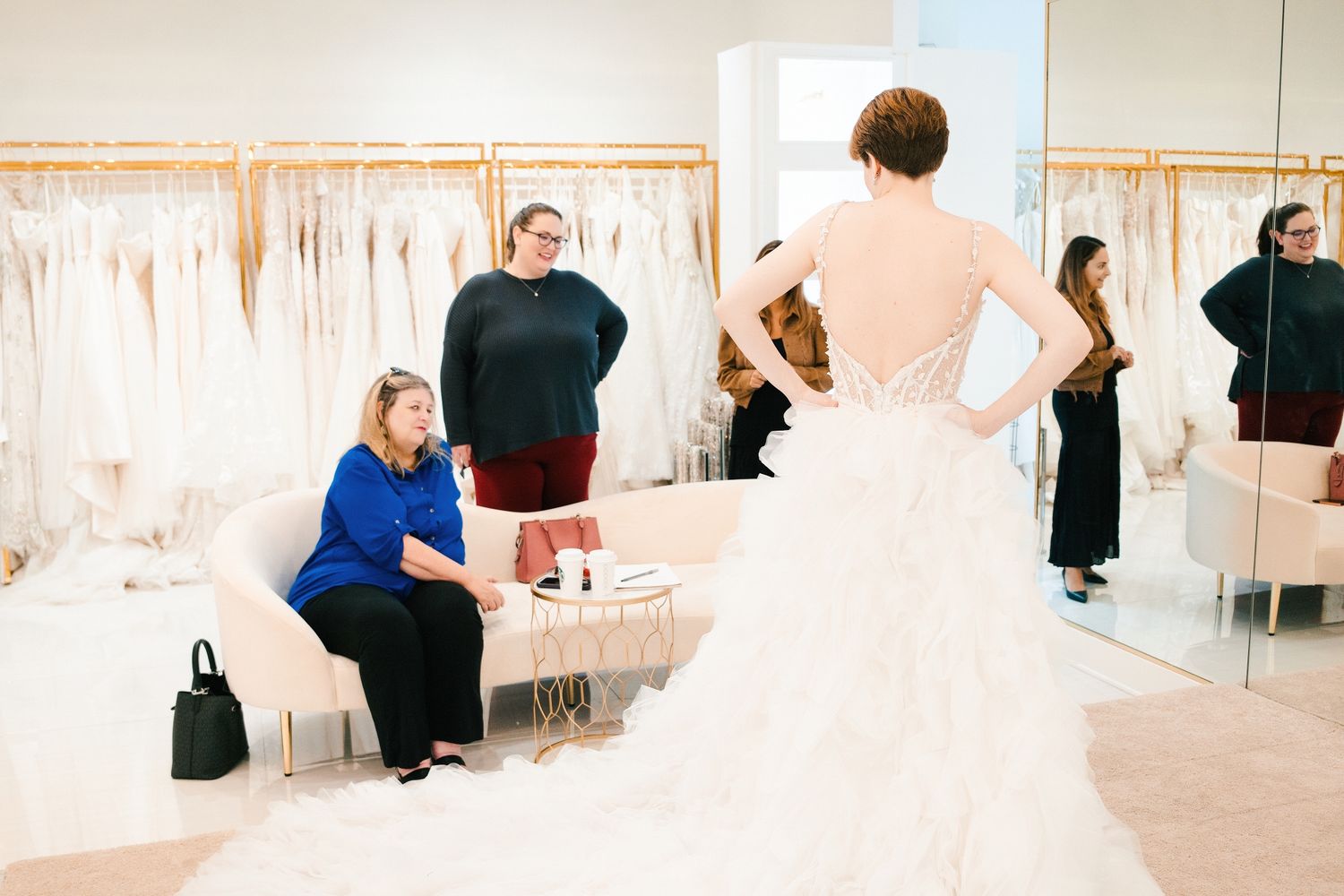 Bridal boutique interior with rows of white wedding dresses displayed on hangers and soft pink walls.