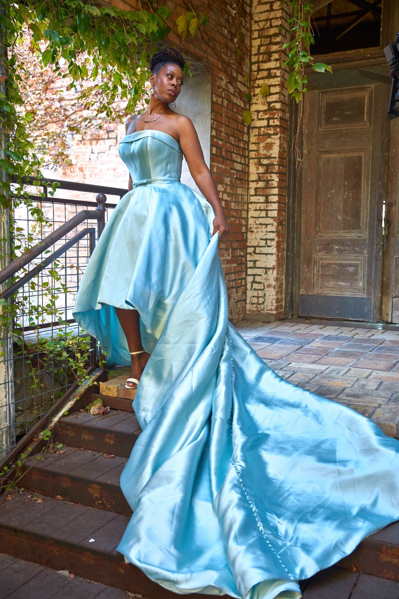 Dramatic light blue satin ball gown with long train on brick staircase.
