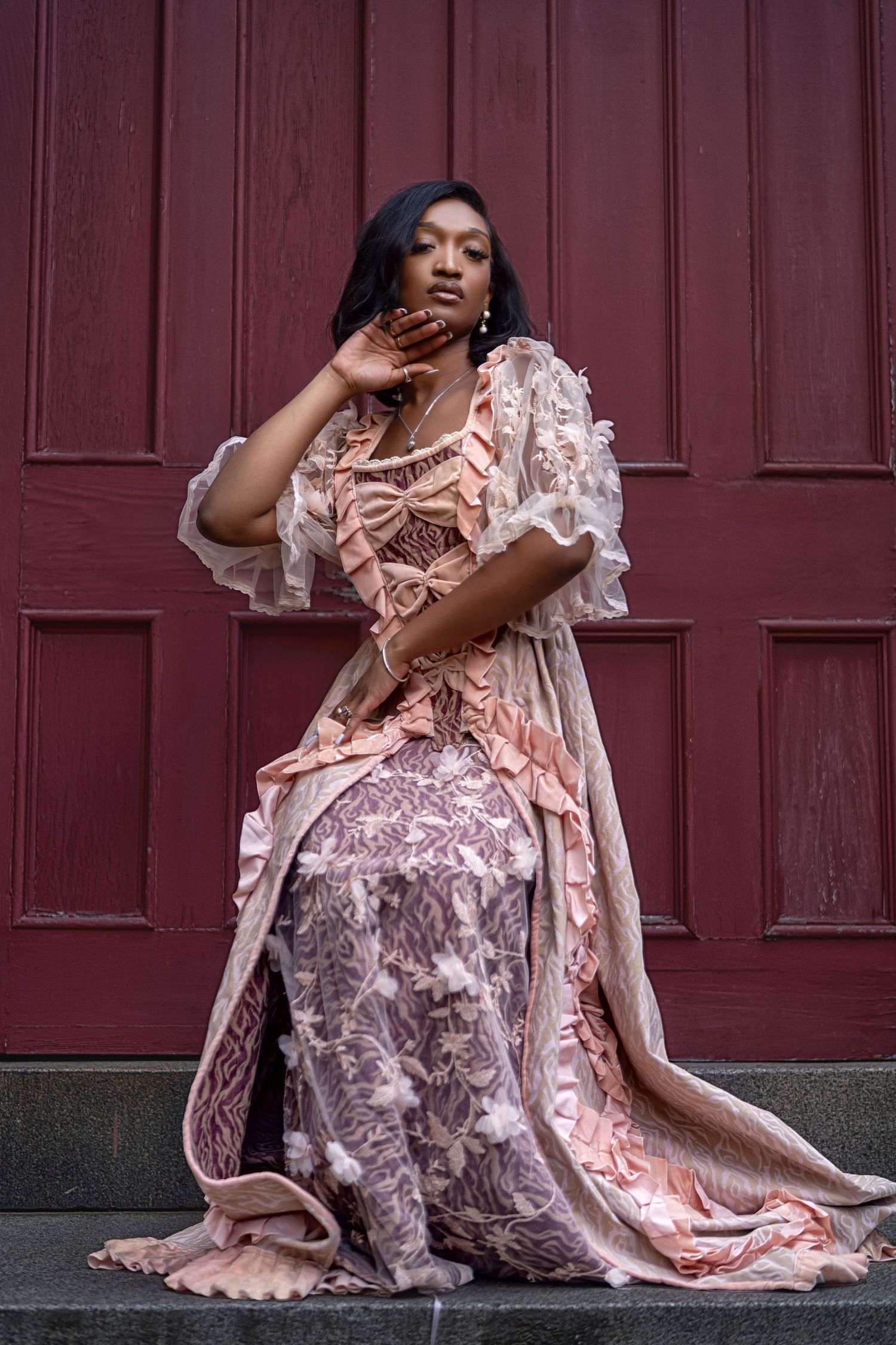 Romantic pink lace dress photographed against deep burgundy wooden doors.