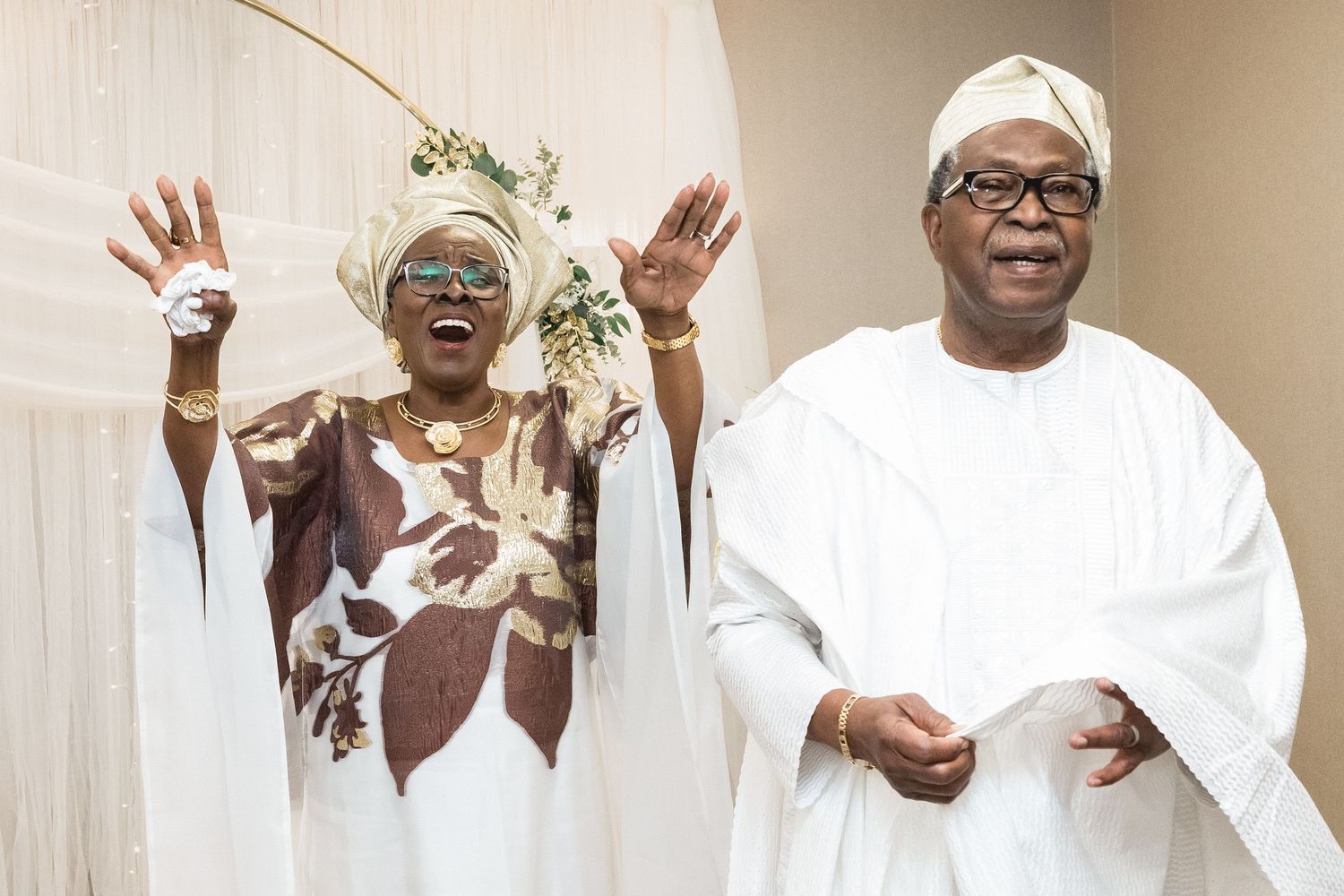 Two people in traditional white African attire share a joyful moment together.
