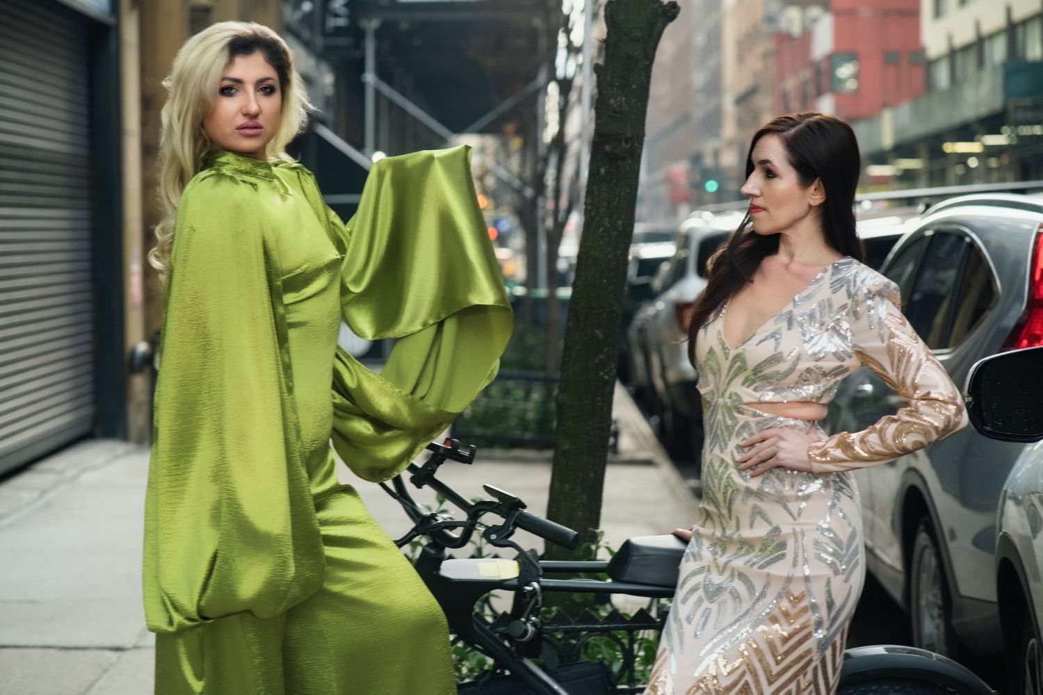 Two models pose on city sidewalk wearing elegant lime green and patterned dresses.