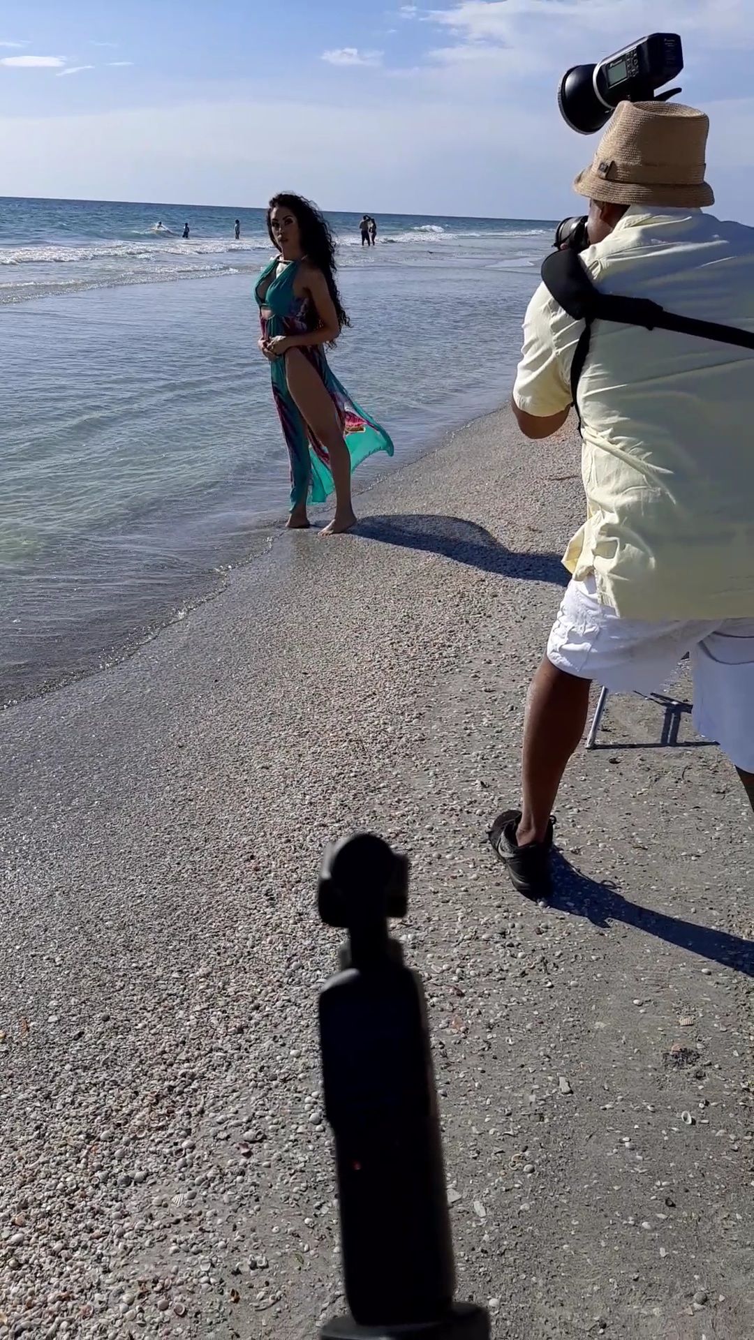 Behind-the-scenes of a beachside photoshoot with photographer and model on shoreline.