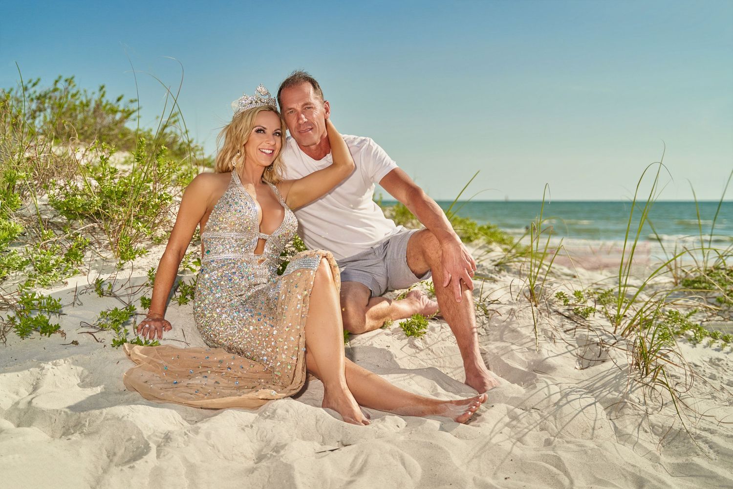 Couple lounging on white sand beach with ocean and dunes in the background.
