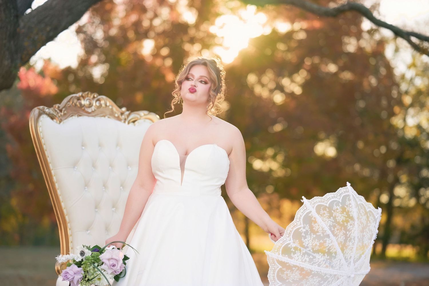 A bride in a white gown poses on an elegant vintage chair at sunset.