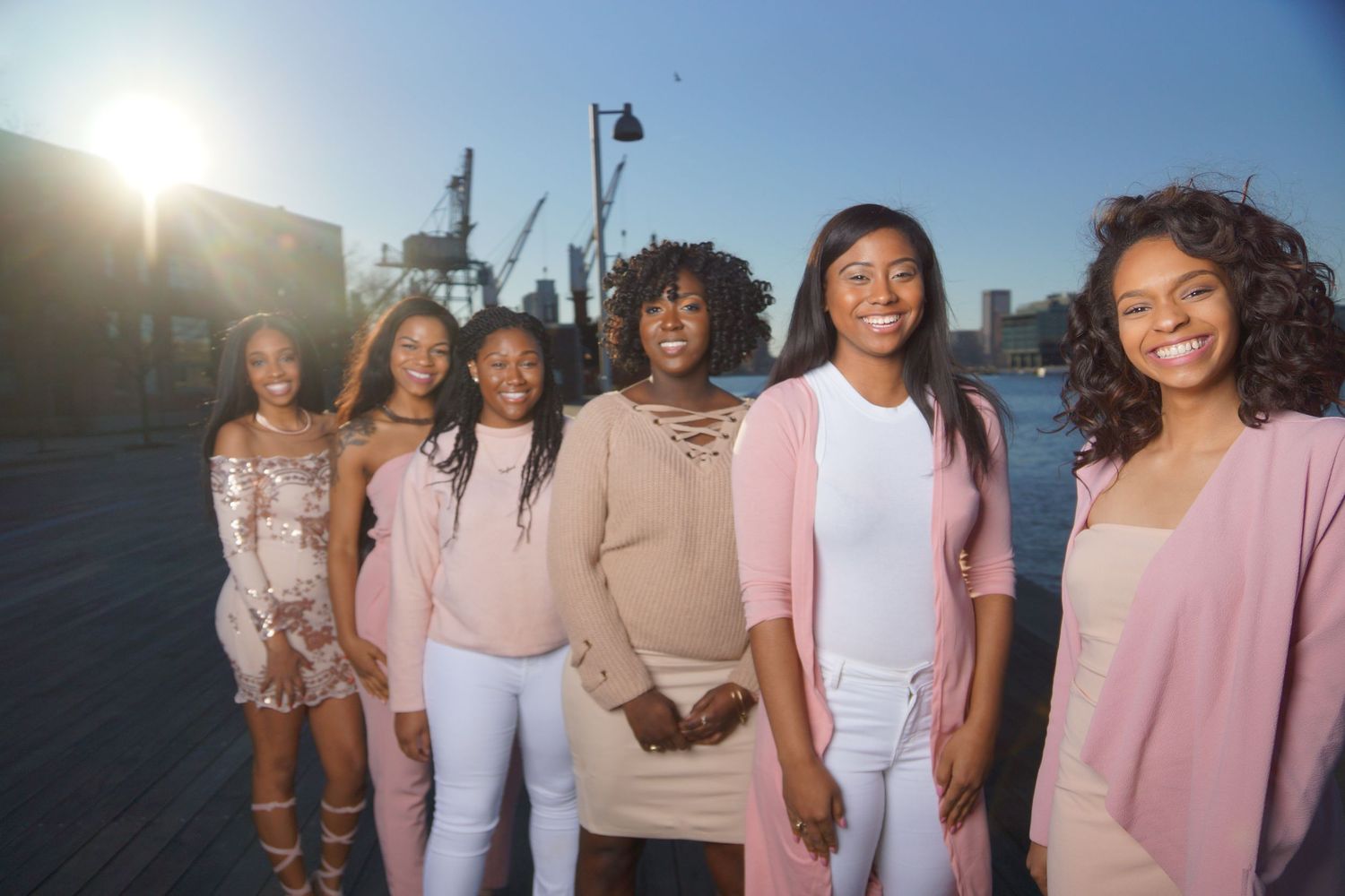 Group wearing coordinated pink and white outfits poses outdoors.