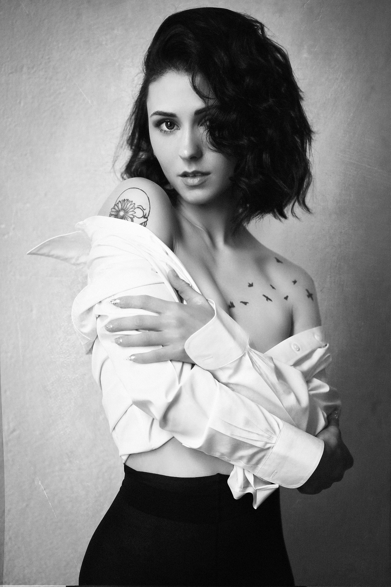 Artistic black and white portrait featuring white ruffled top and small bird tattoos.