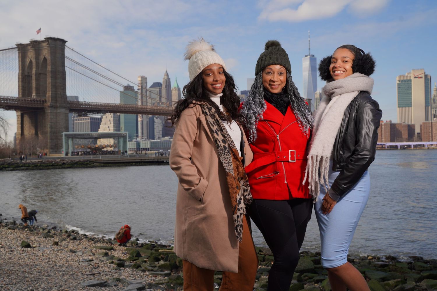 Three friends enjoying a winter day by the Brooklyn Bridge with the NYC skyline in the background.