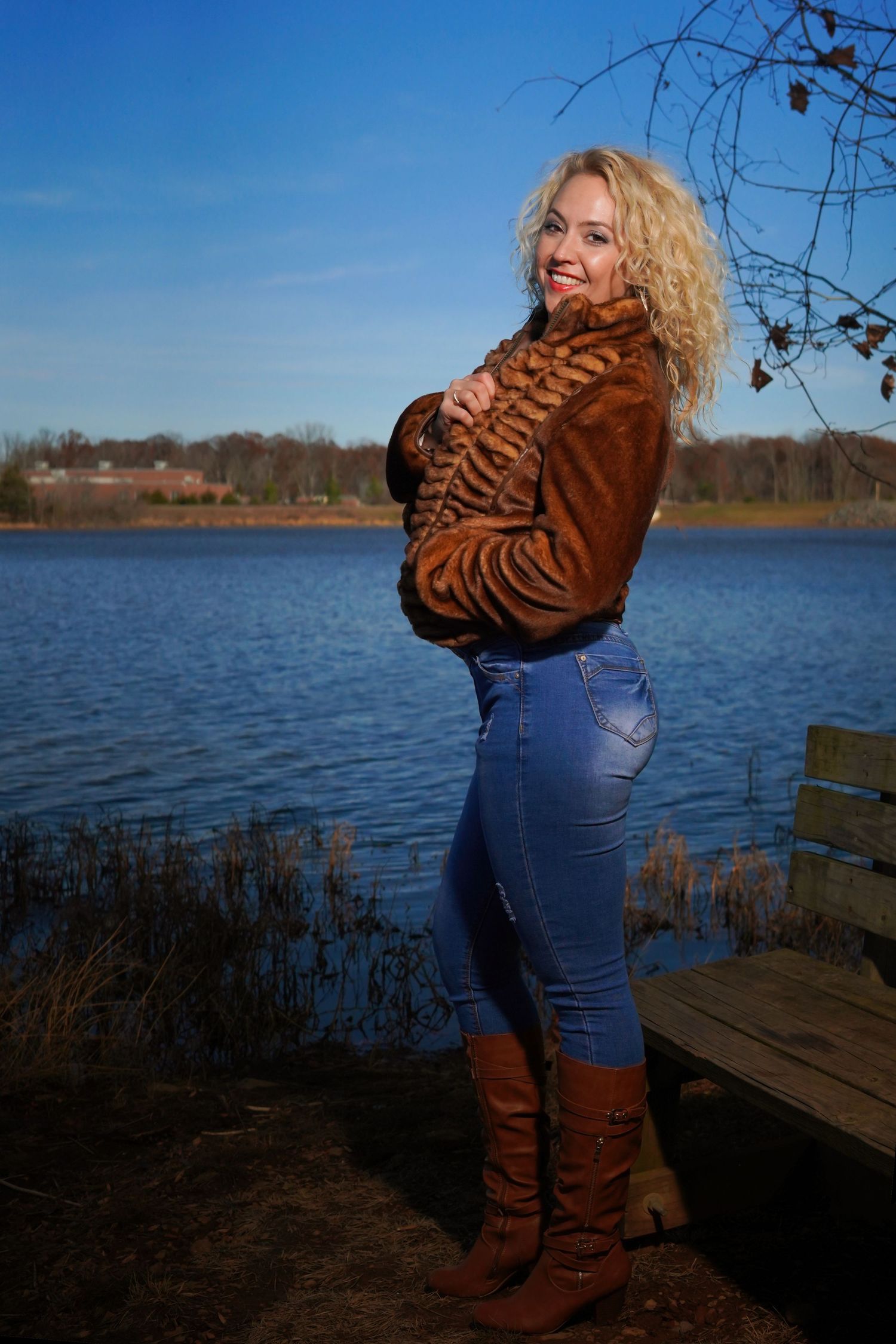 Casual portrait by lake wearing brown sweater, jeans and boots.