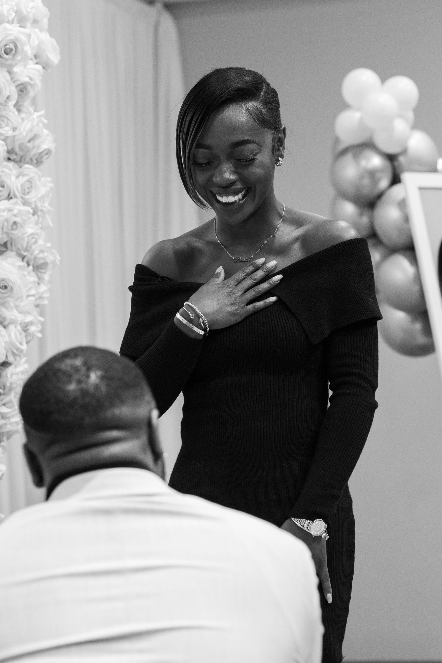 Emotional reaction during surprise proposal with floral arch and balloons in background.