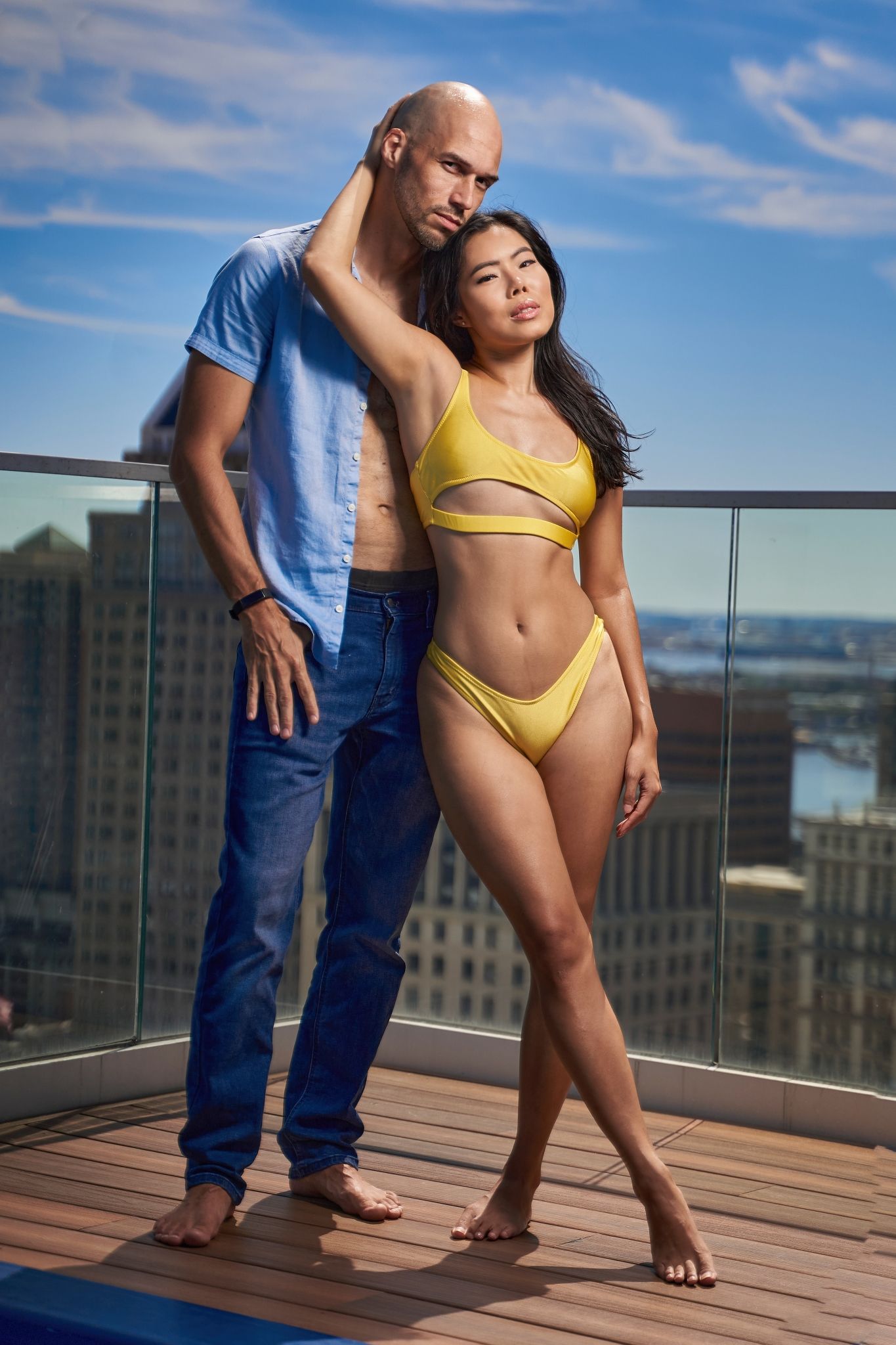 Outdoor photoshoot on a wooden deck with blue sky and urban backdrop.