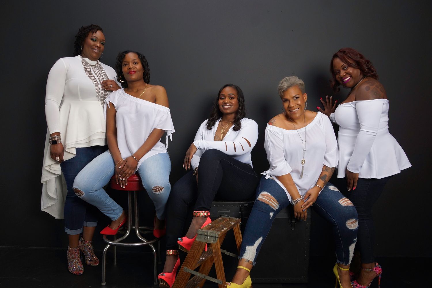 Five women in white tops strike casual poses against dark background.