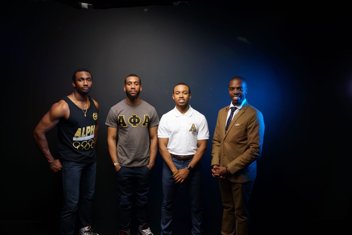 Four men pose together against a dark backdrop with dramatic blue lighting.