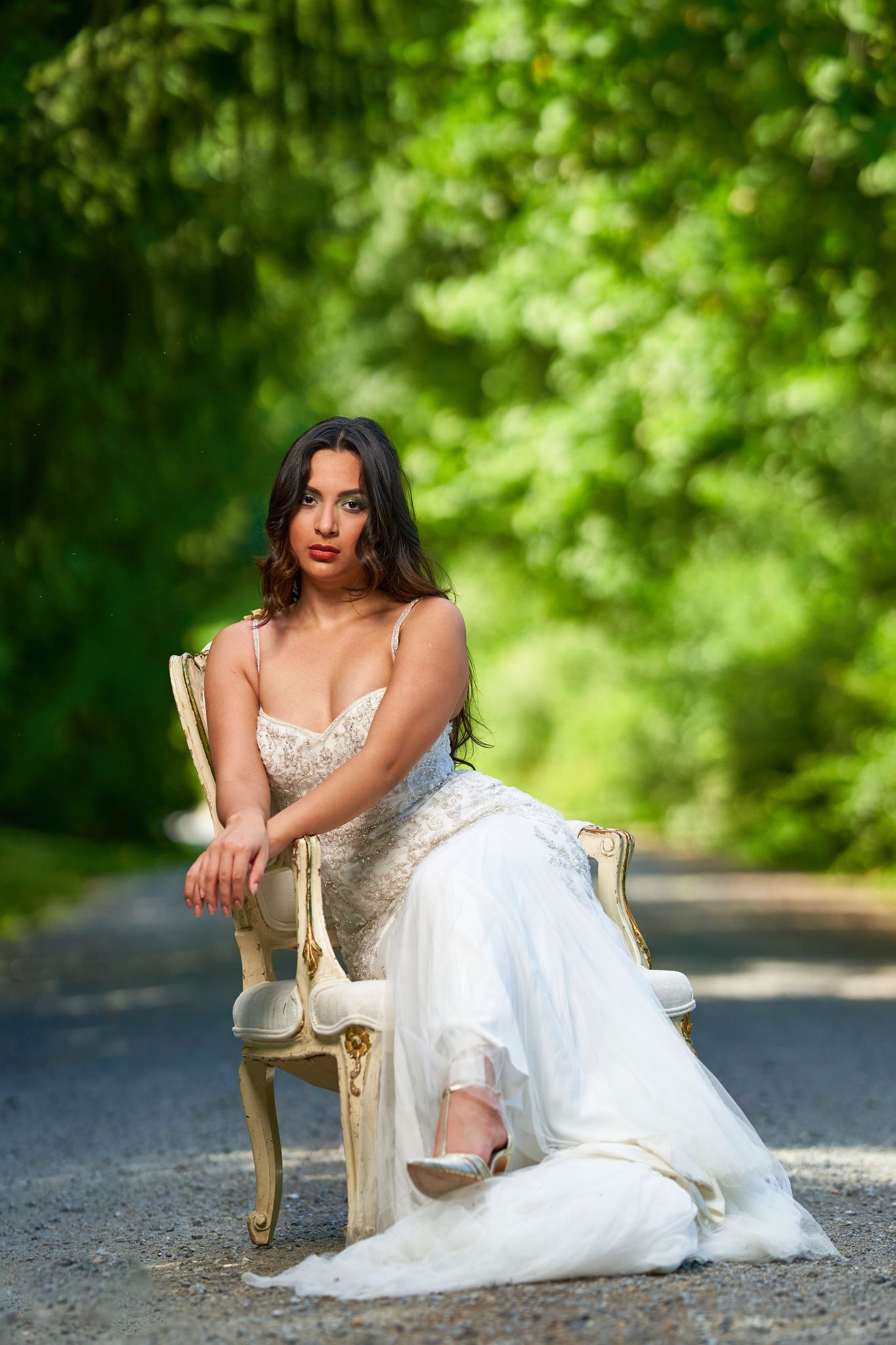 A white wedding gown with delicate details photographed against vibrant green foliage outdoors.