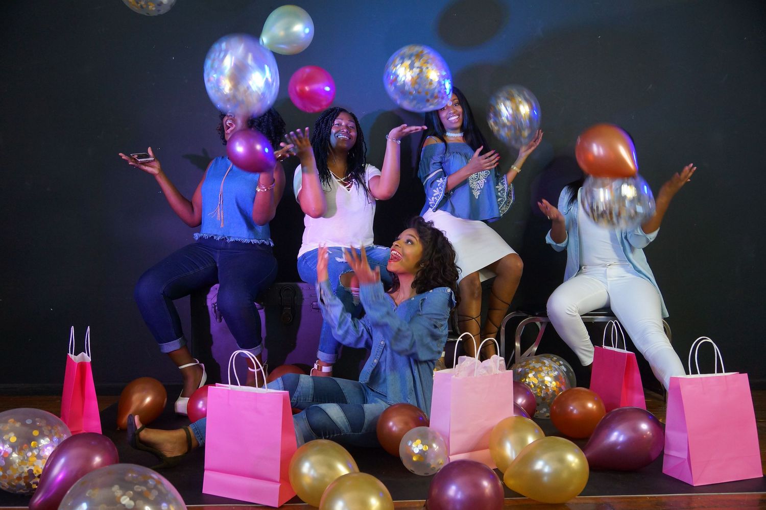 Group celebrates with balloons and shopping bags against colorful backdrop.