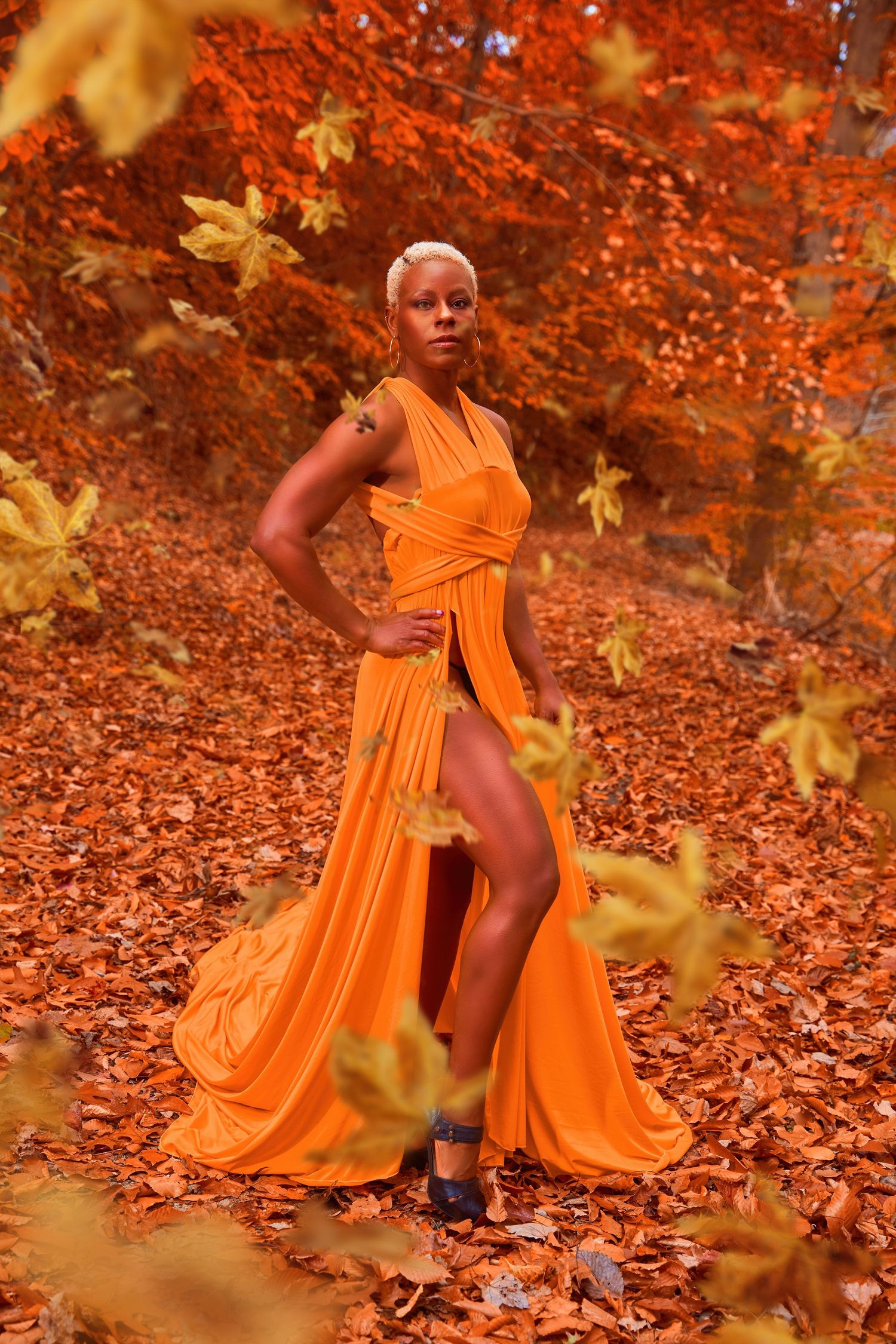 Vibrant orange gown contrasts with autumn foliage in dramatic fashion photo.