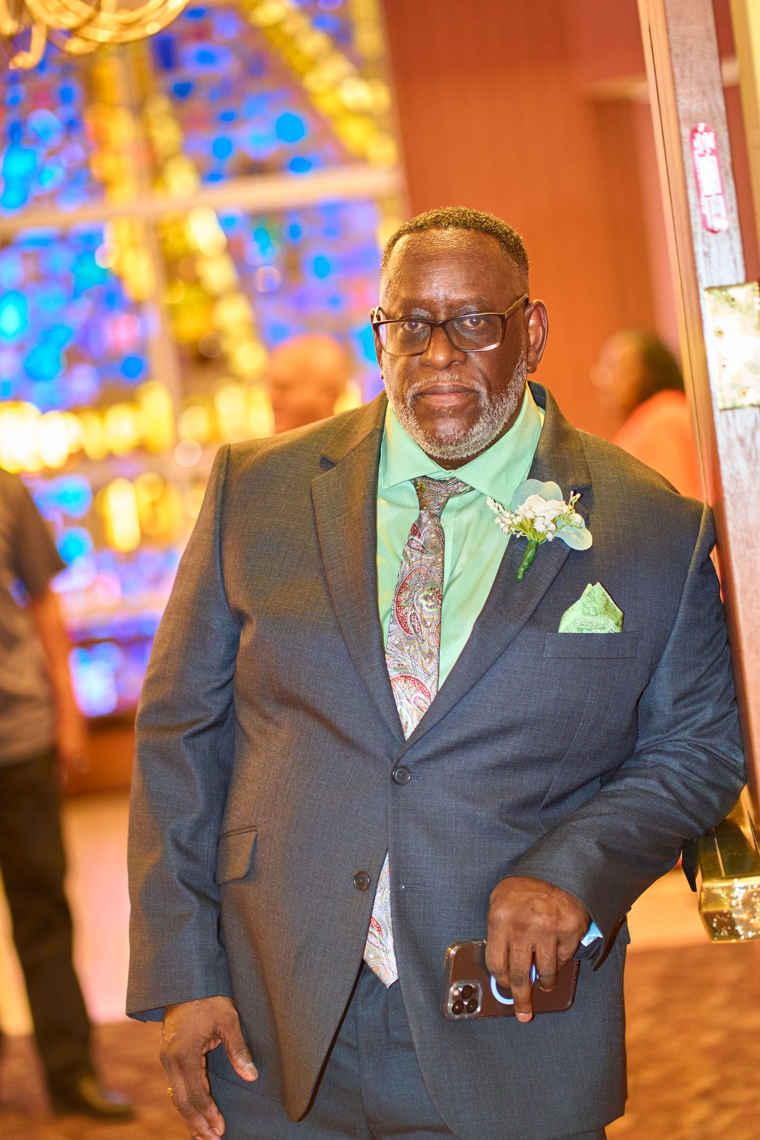 Wedding guest in navy suit with mint green tie and boutonniere smiles in warm lighting.