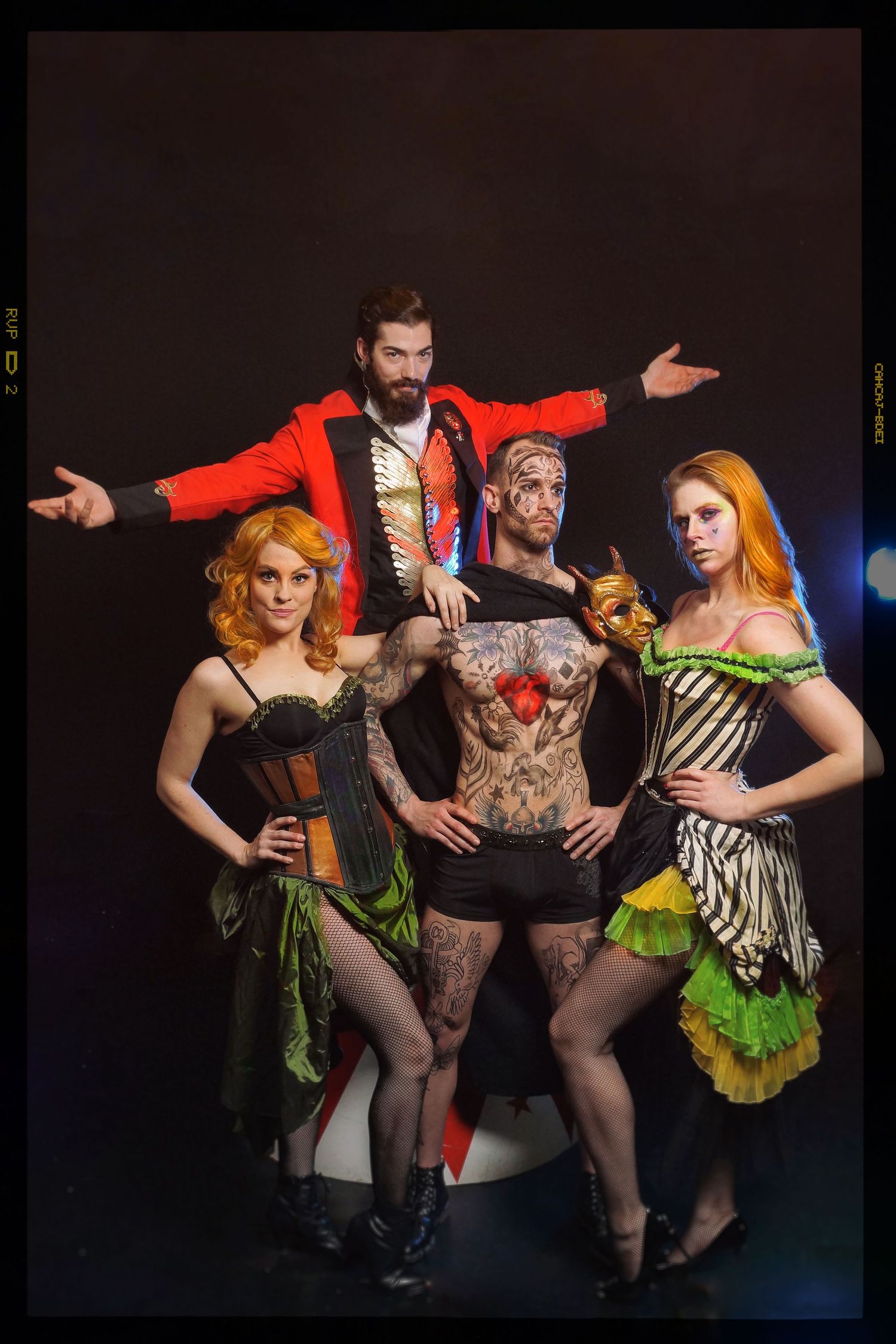 Burlesque performers in colorful costumes posing dramatically on dark stage.