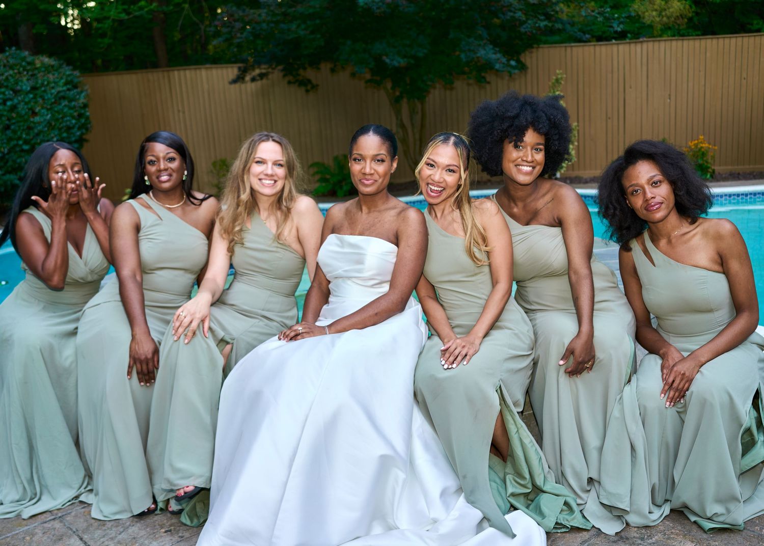 Bridesmaids in mint green dresses and bride in white gown pose together outdoors.