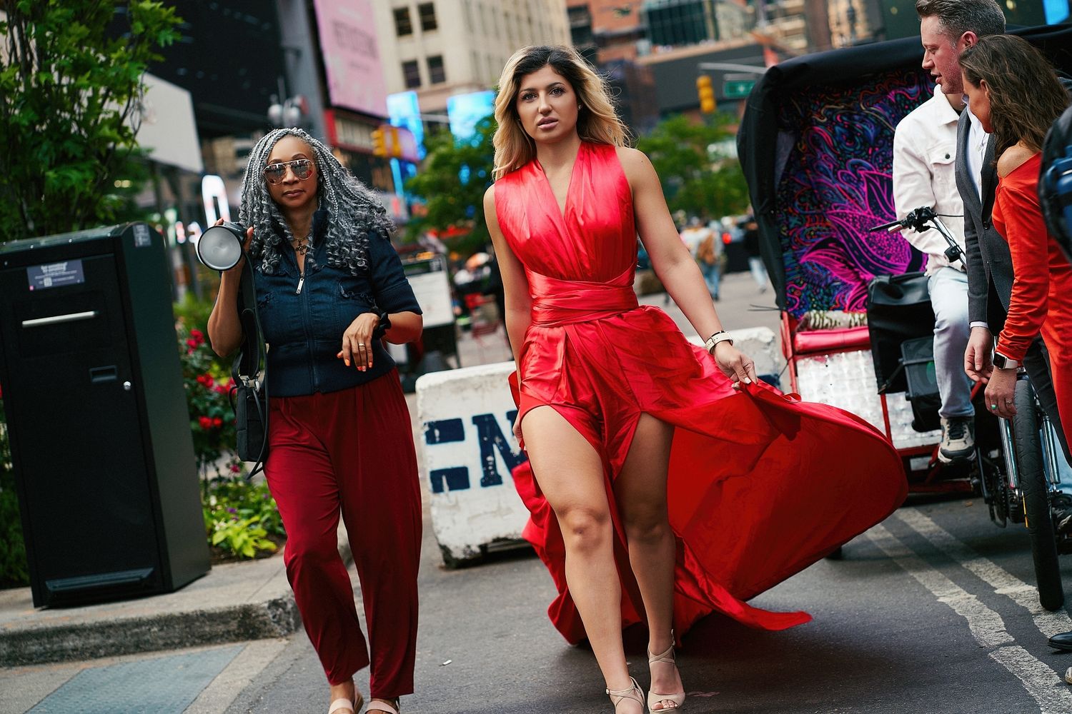 A flowing red dress billows dramatically on a city street during a fashion photoshoot.