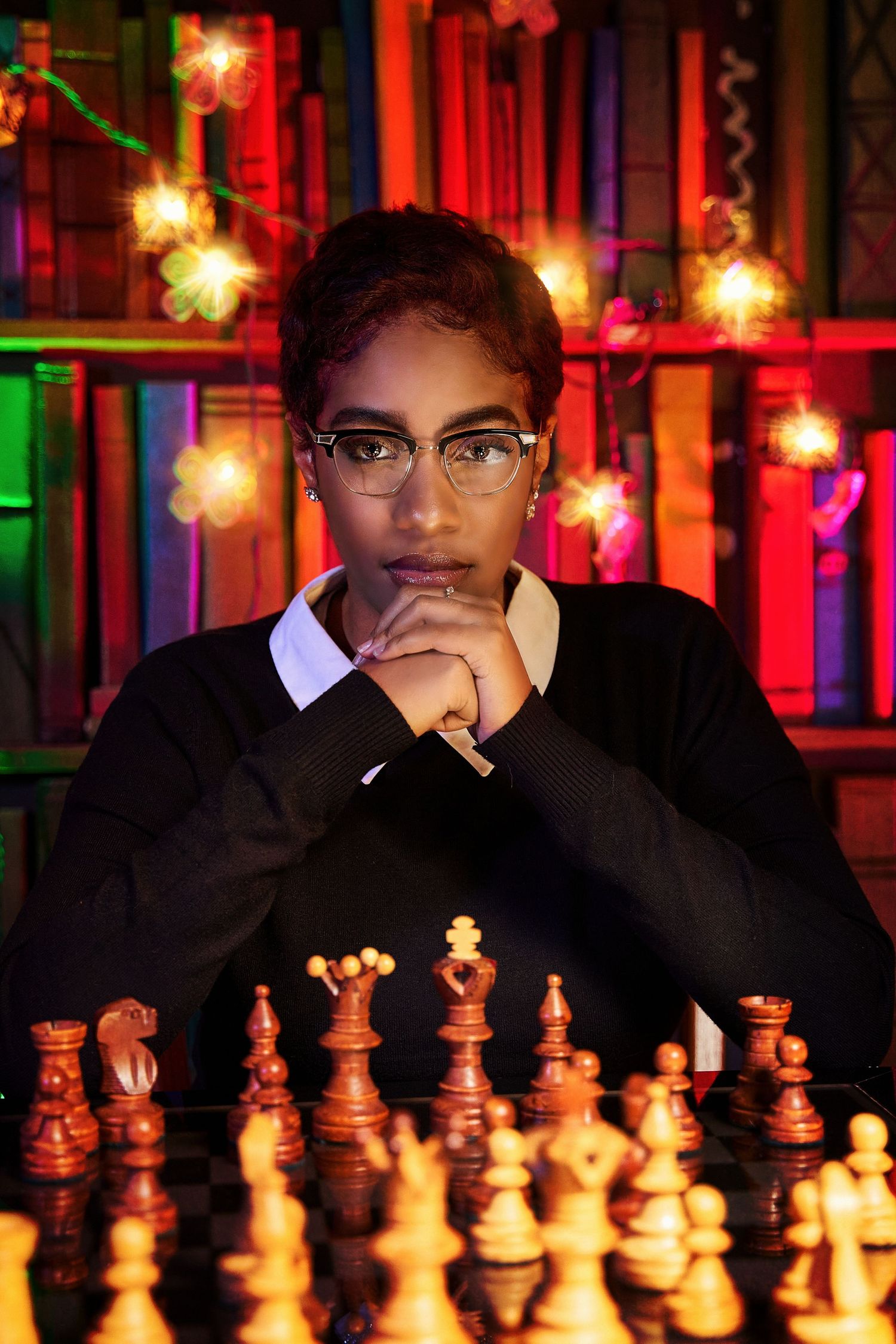 Dramatic portrait with chess pieces in foreground against colorful bookshelf lighting.