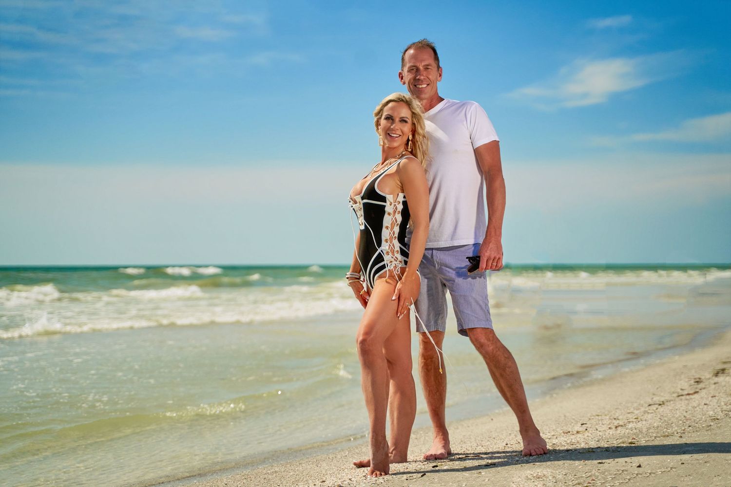 Couple walking along pristine beach shoreline with turquoise waters in the background.