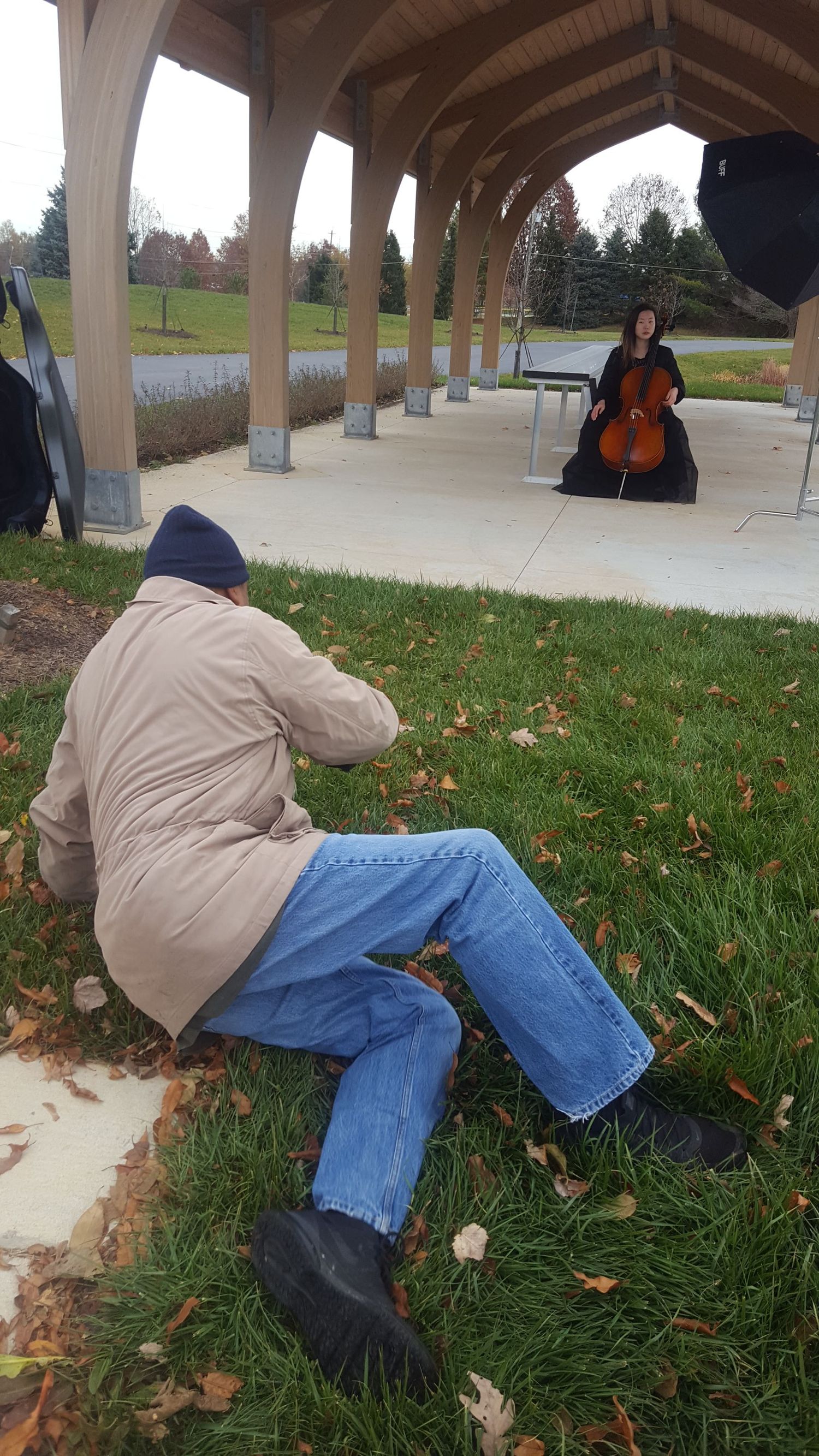 Photographer capturing musician playing cello under covered outdoor walkway.