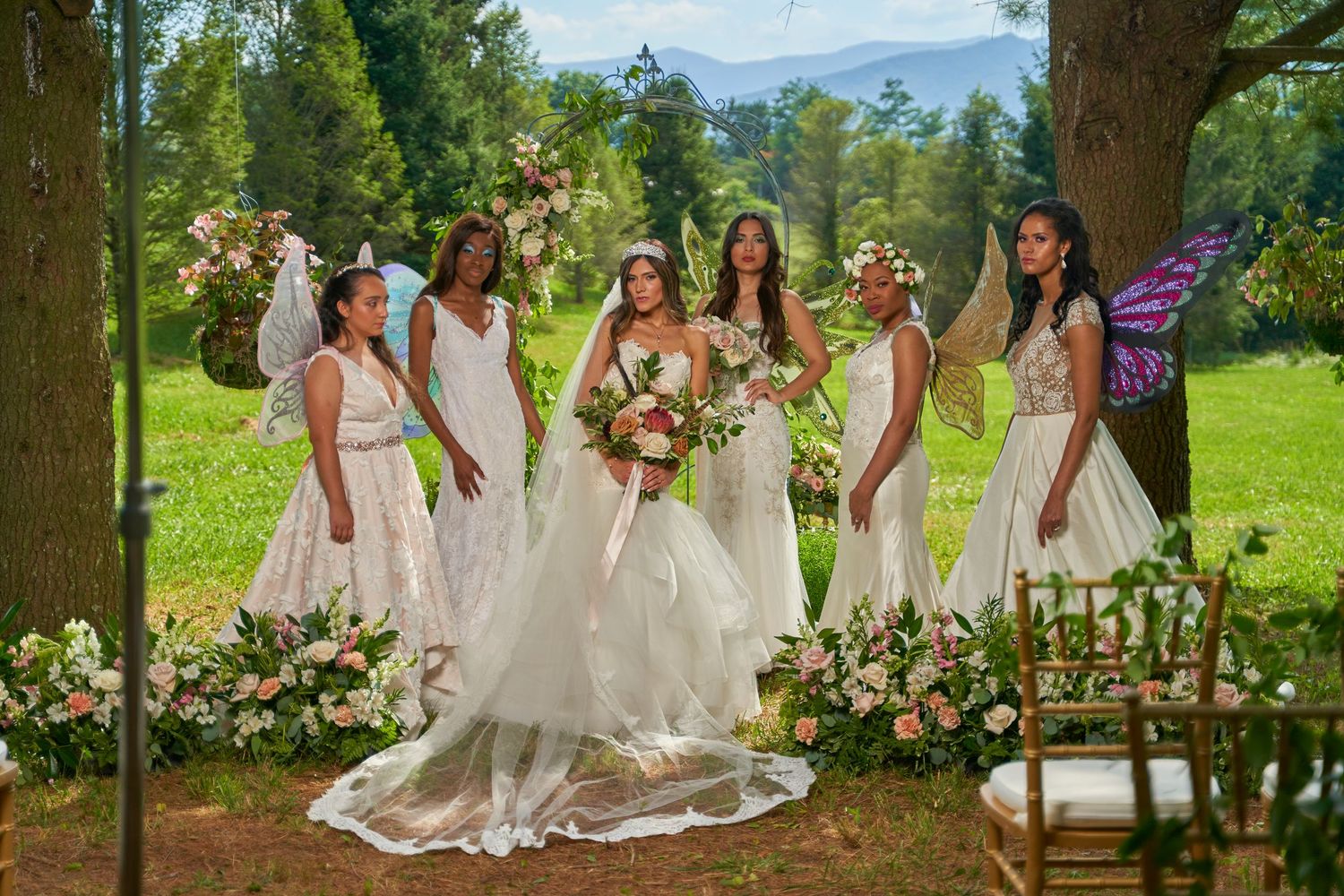 Bridal party in flowing white dresses poses together in a scenic garden setting.
