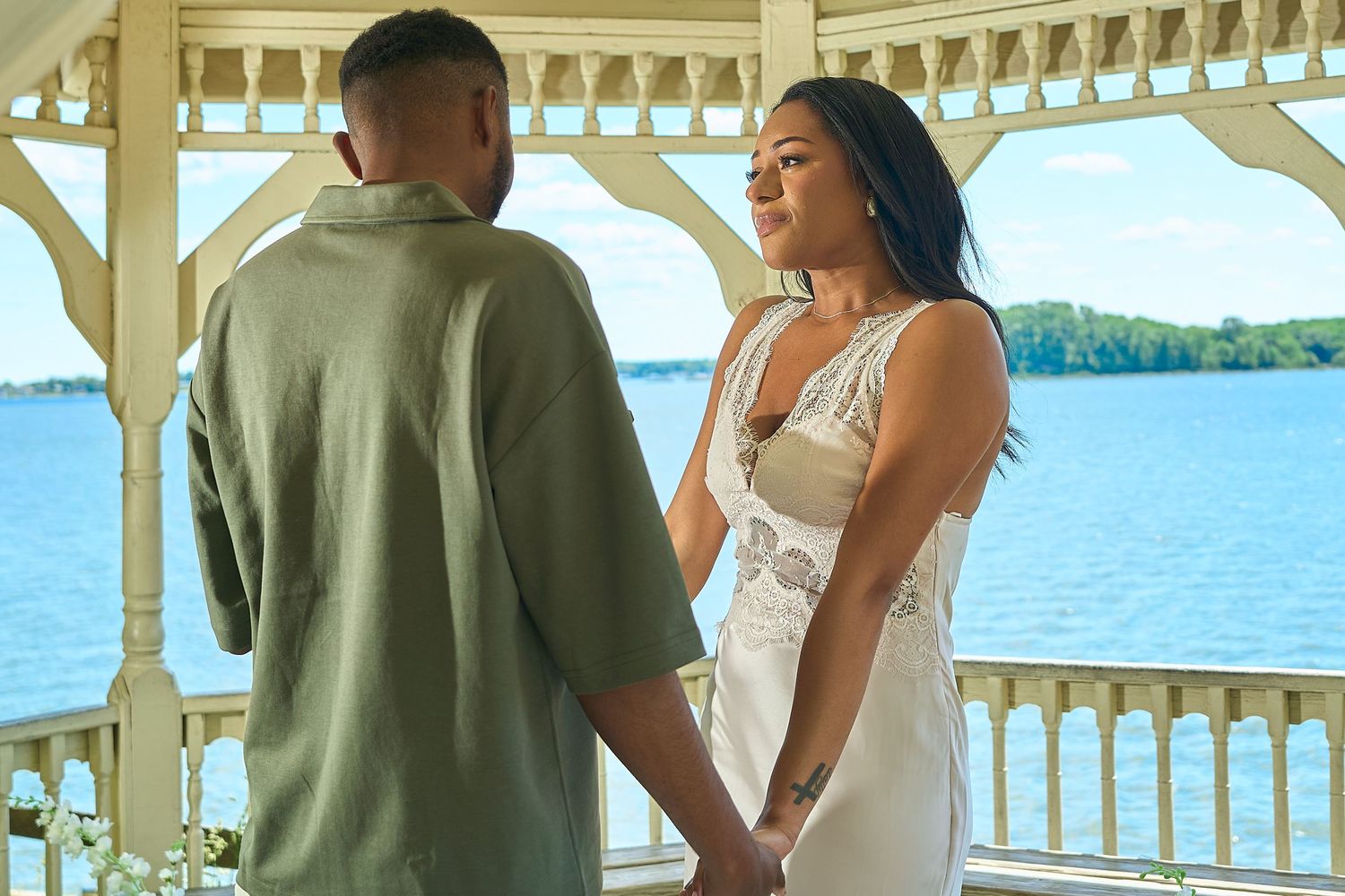 Couple holding hands in a white gazebo overlooking a serene lake on a sunny day.