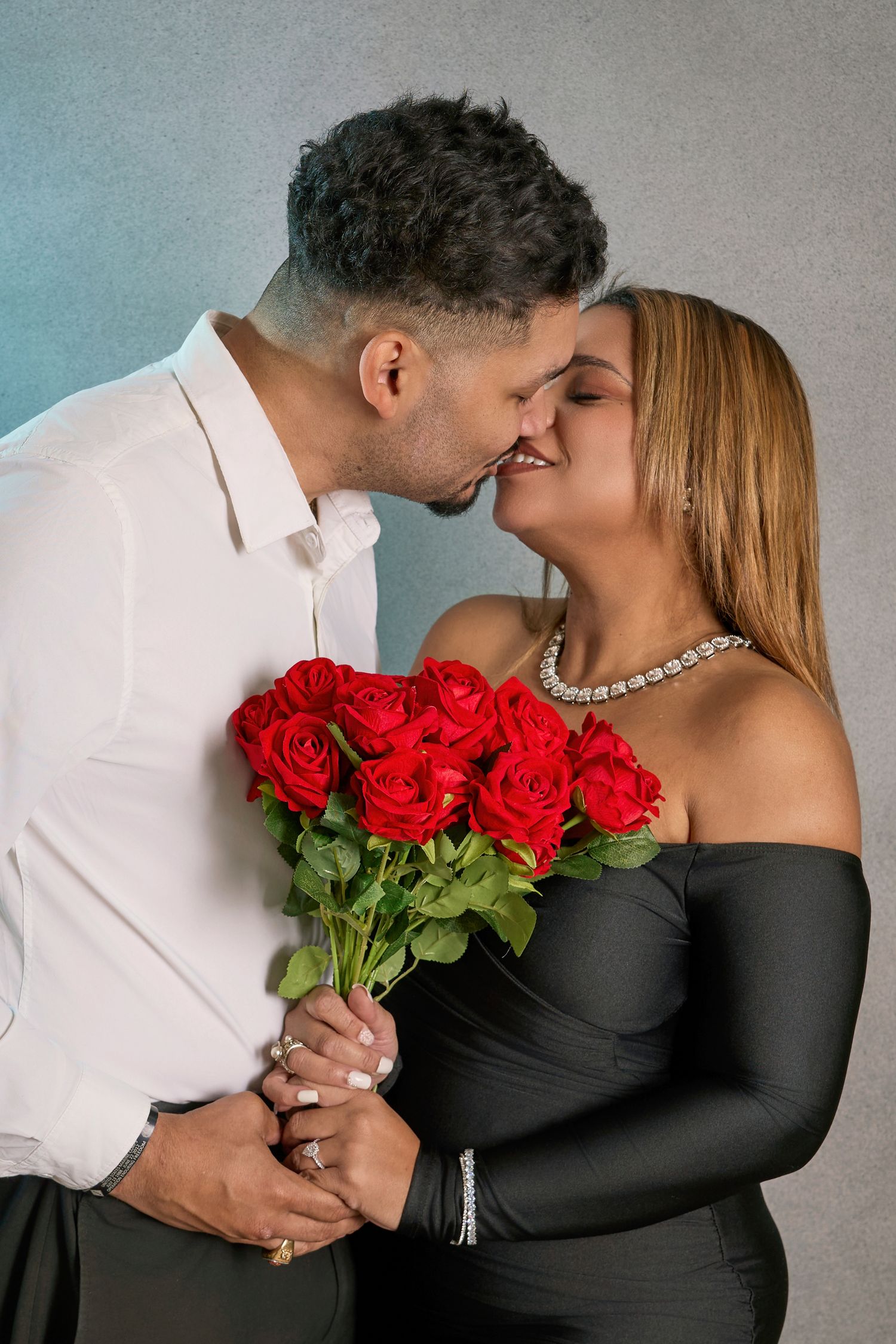 Romantic couple embracing while holding red roses against grey background in series of intimate portrait shots.