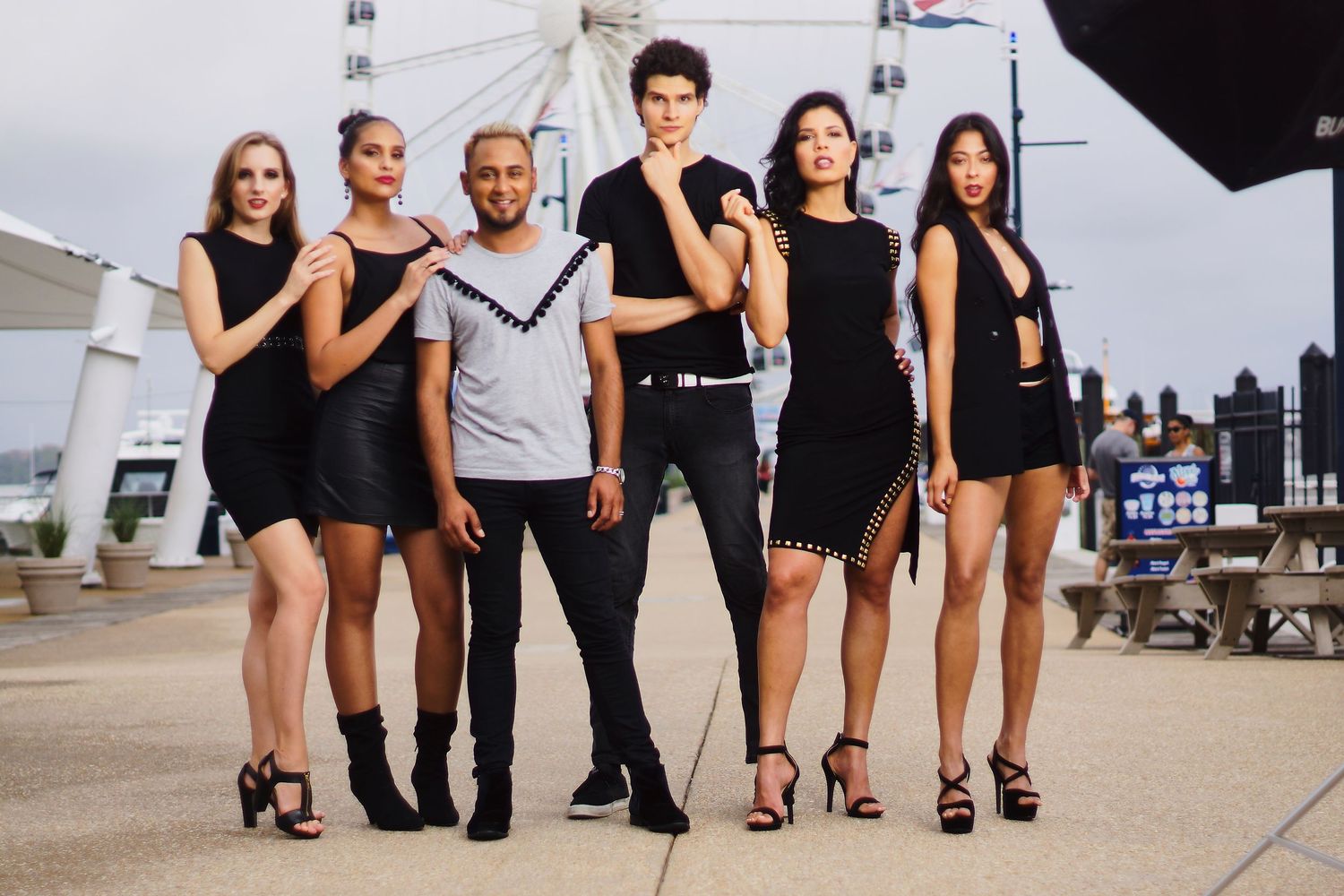 Models in coordinated black outfits posing for a photoshoot near a ferris wheel.