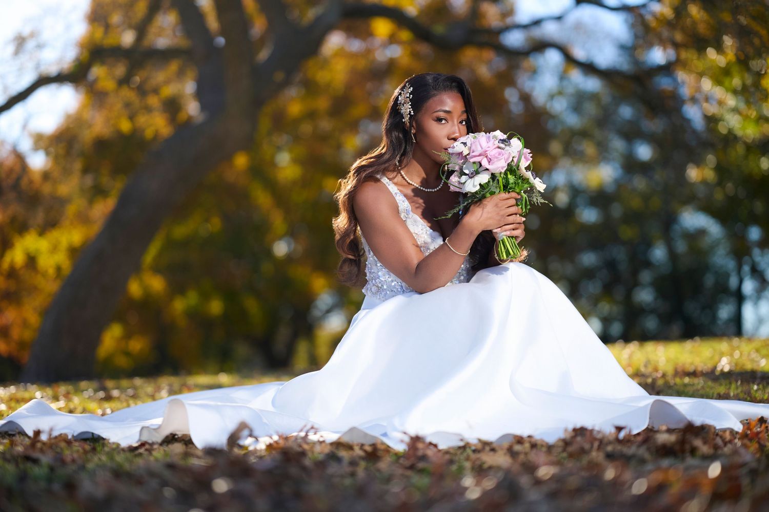 White wedding dress photographed among fallen autumn leaves outdoors.